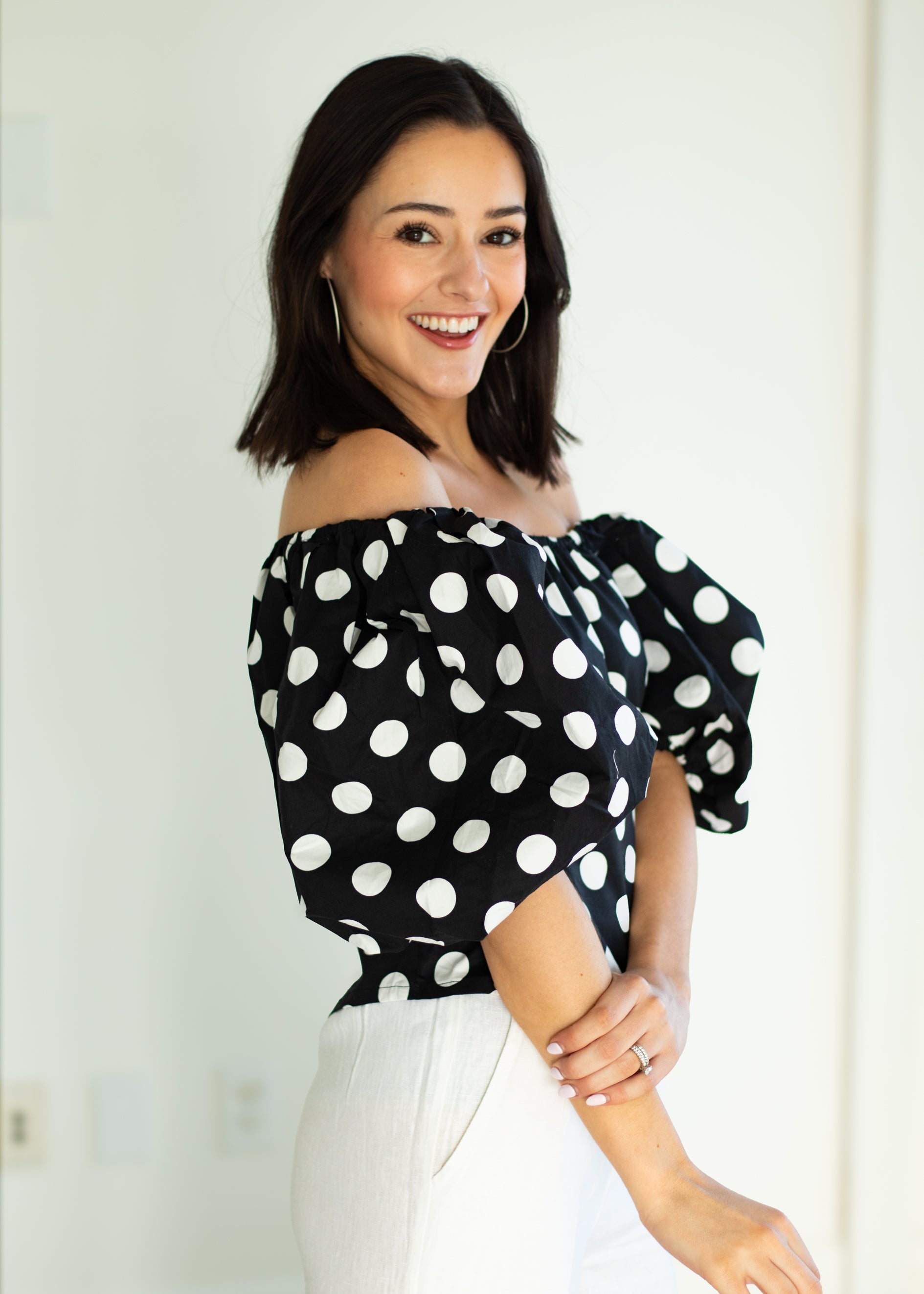 Woman wearing a black polka dot top with white pants against a light background