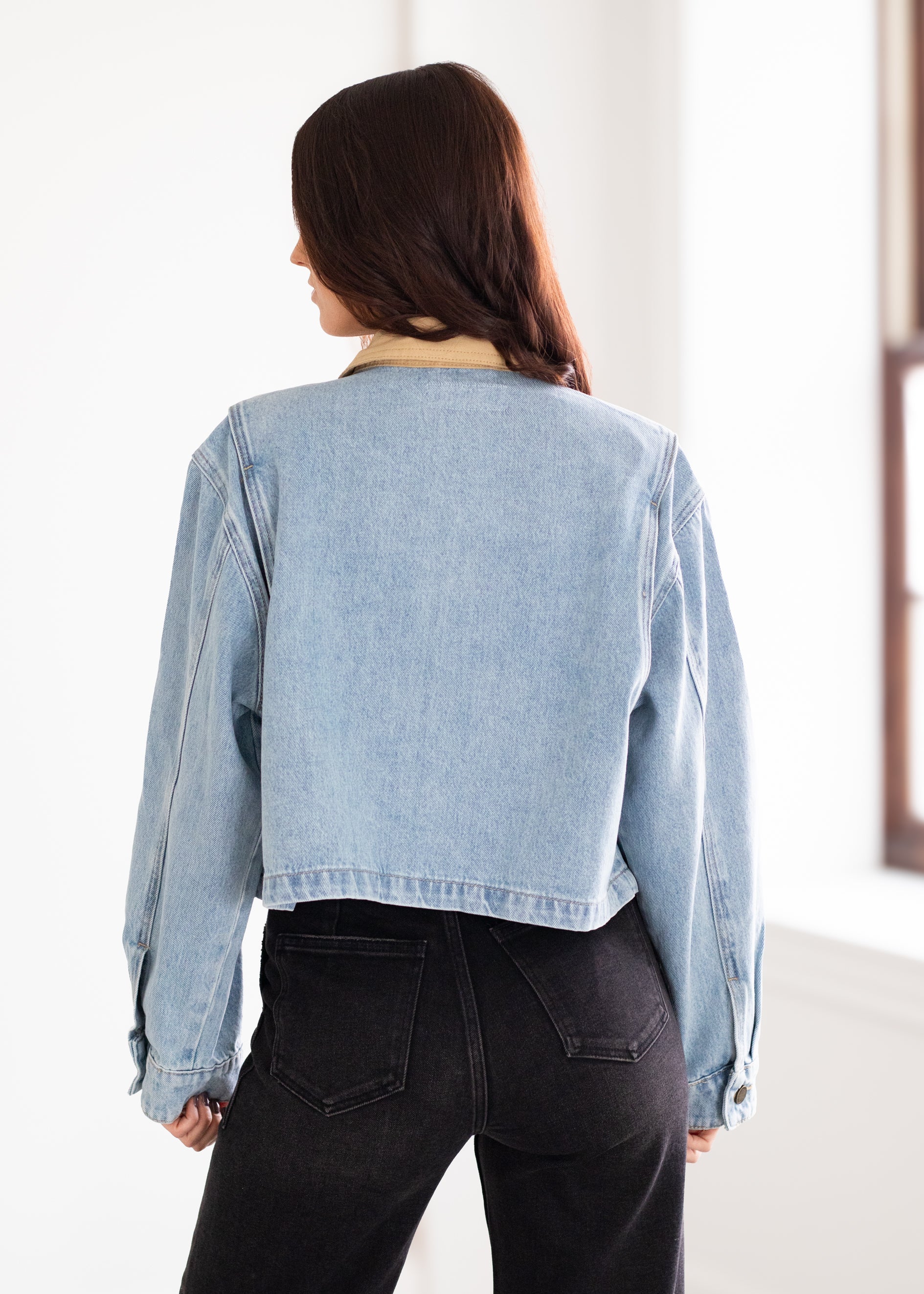 Person wearing a light blue denim jacket and black pants in a bright room.