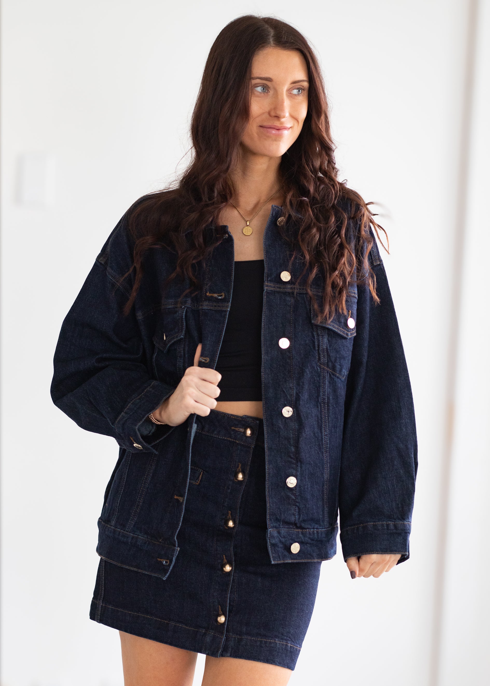 Woman wearing a dark denim jacket and skirt on a white background