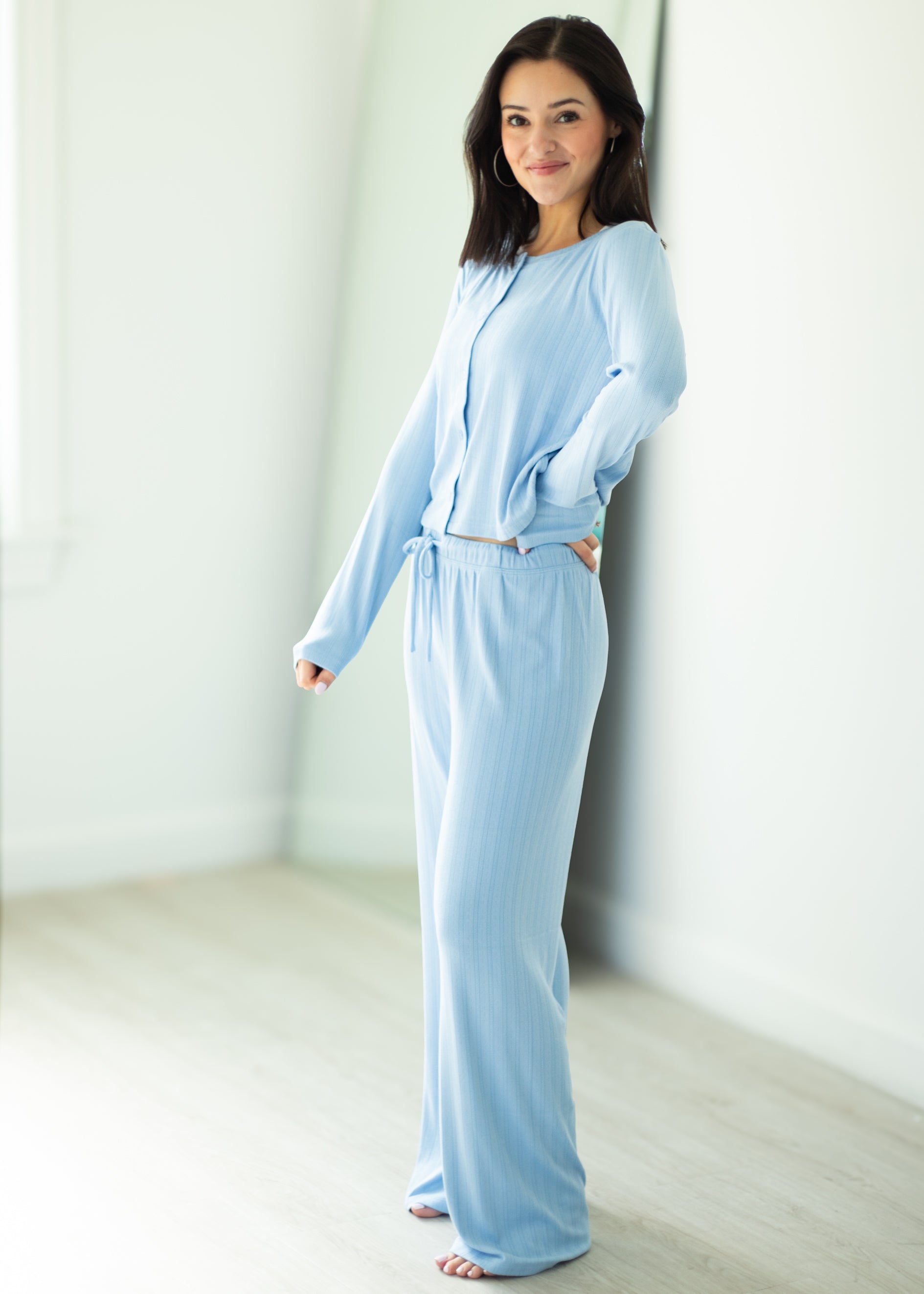 Woman wearing a light blue pajama set in a minimalistic room.