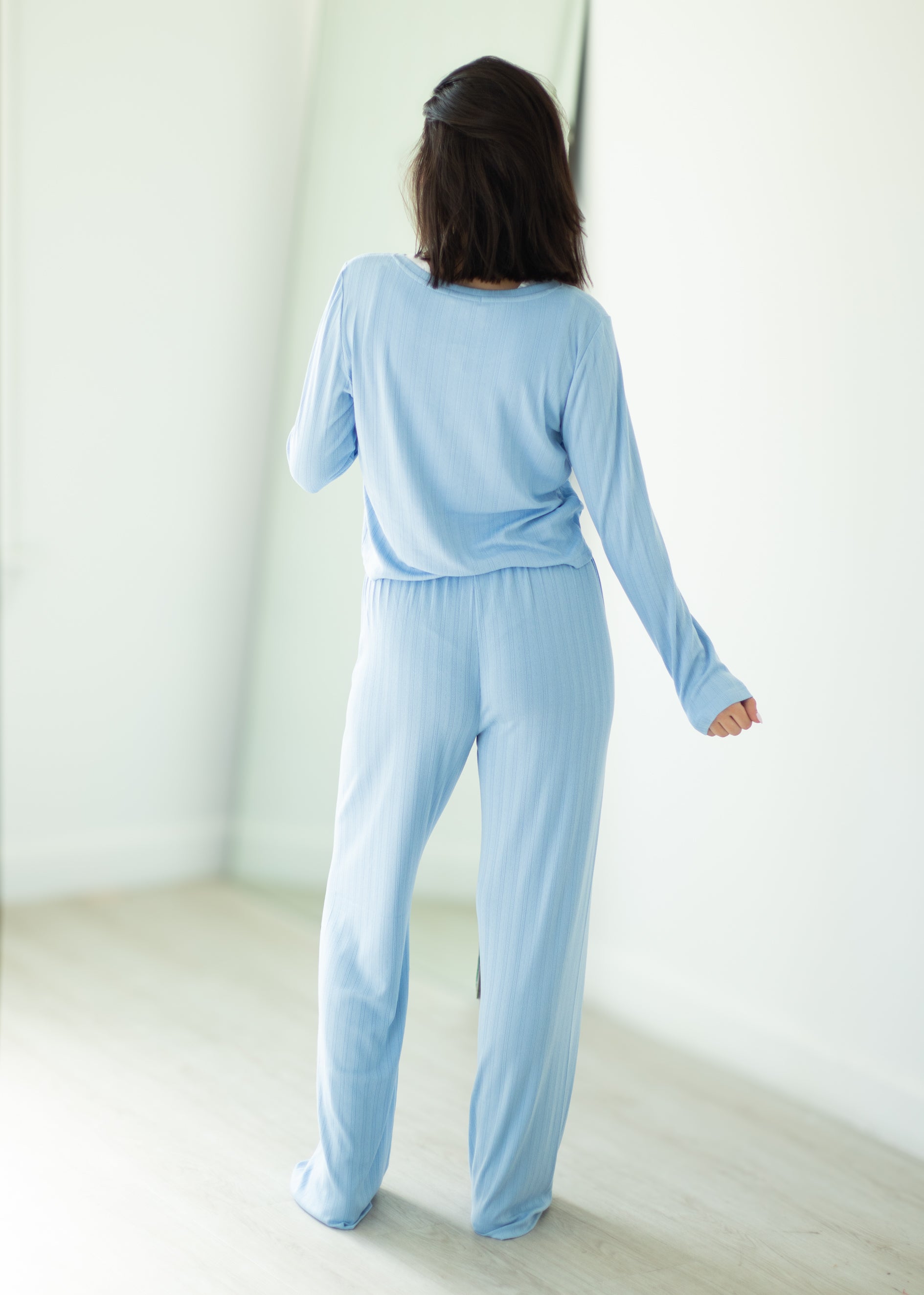Woman wearing a light blue pajama set standing in a minimalistic room.