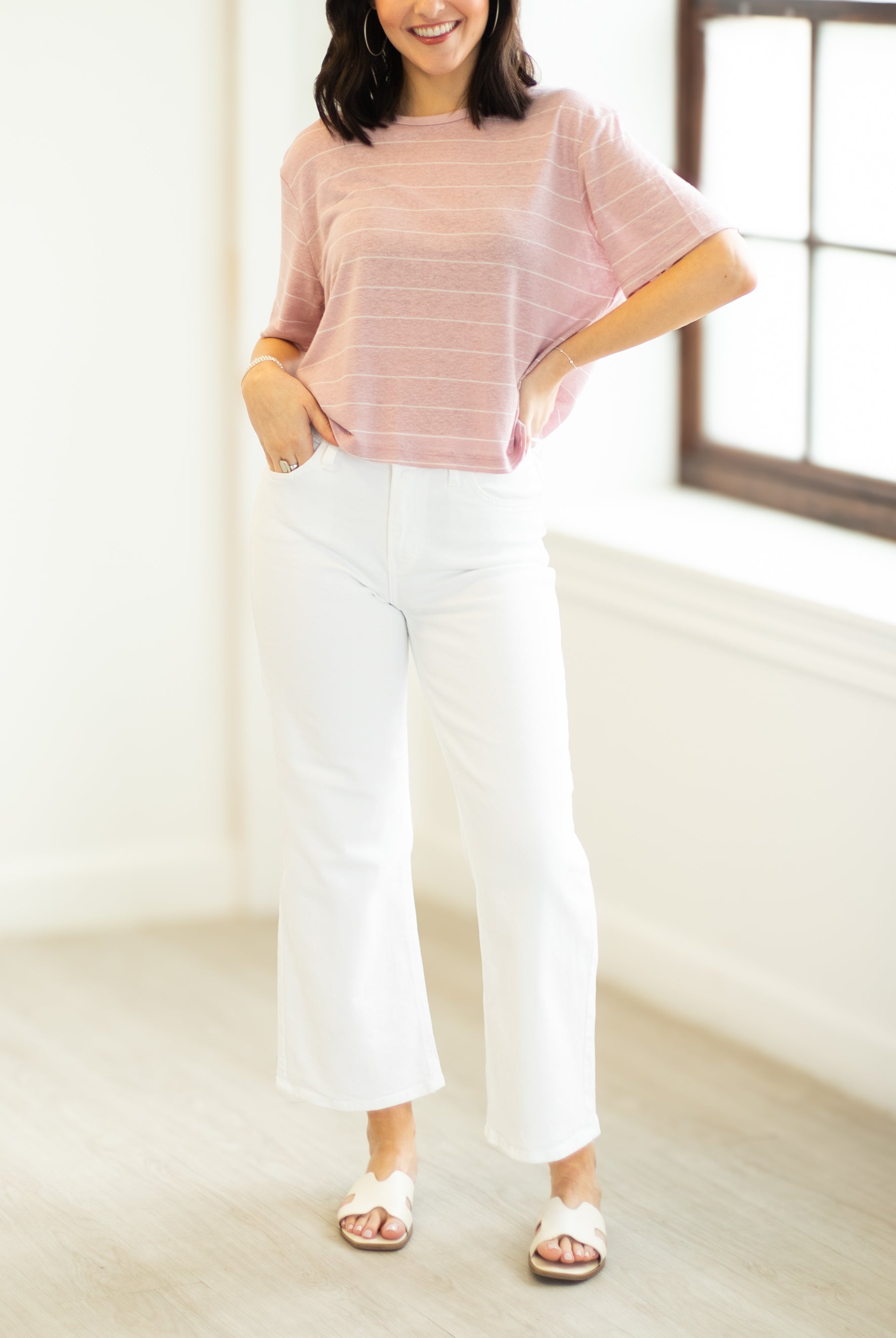 Woman wearing a pink striped shirt and white pants in a bright room.
