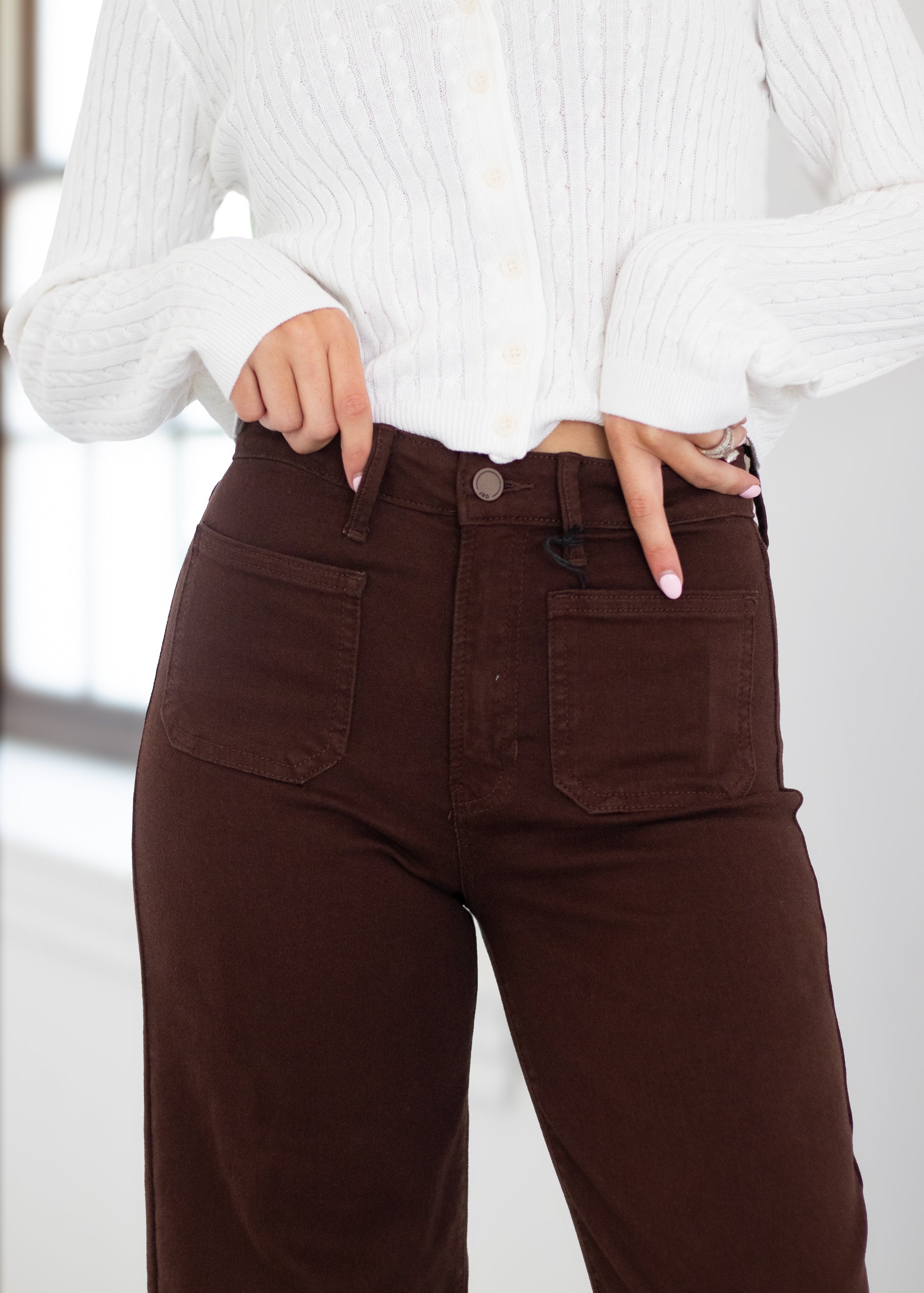 A person wearing dark brown high-waisted corduroy pants with front patch pockets, paired with a white ribbed knit top.
