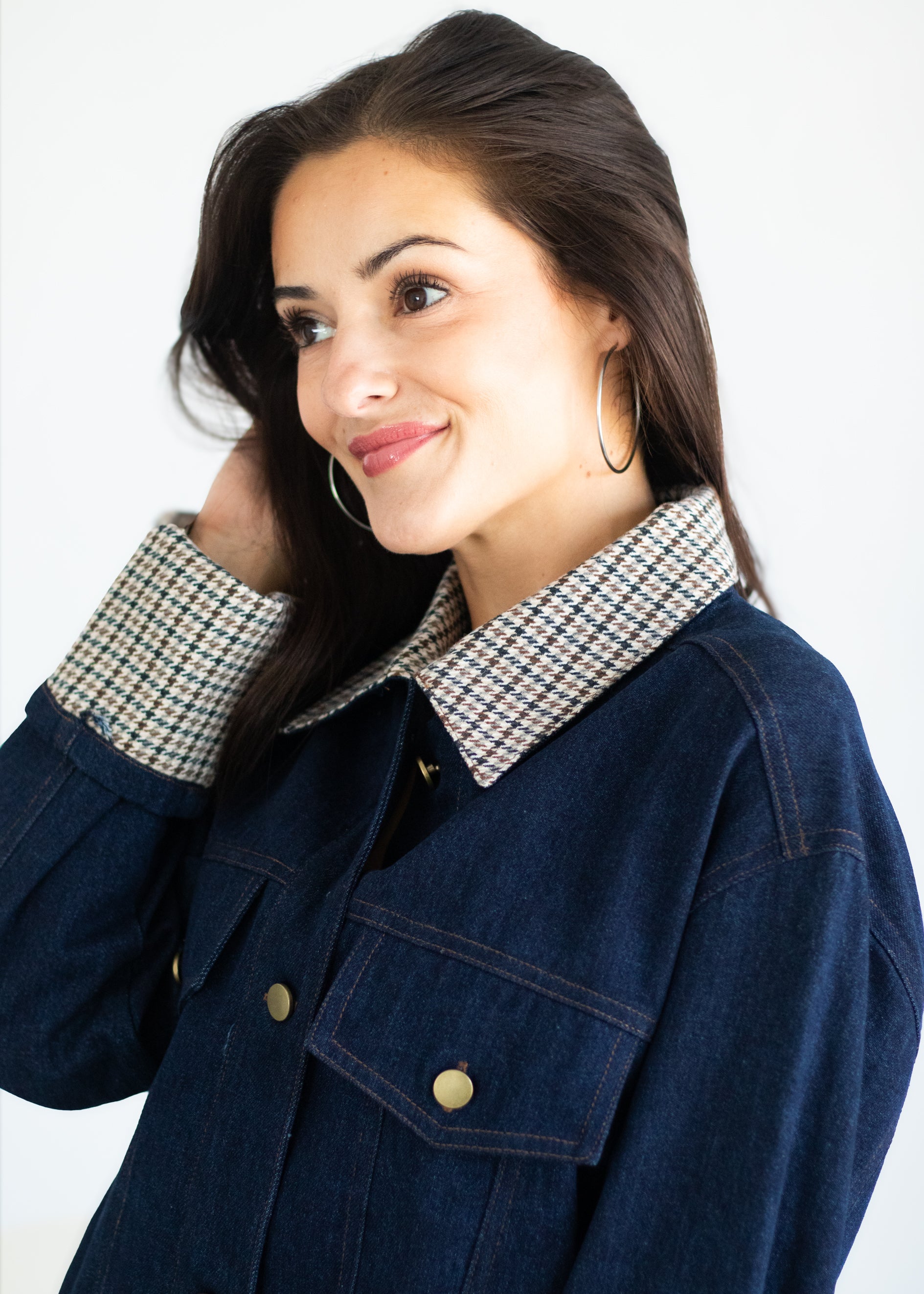 A woman wearing a dark blue denim jacket with a contrasting beige and black houndstooth patterned collar, posed against a clean white background.