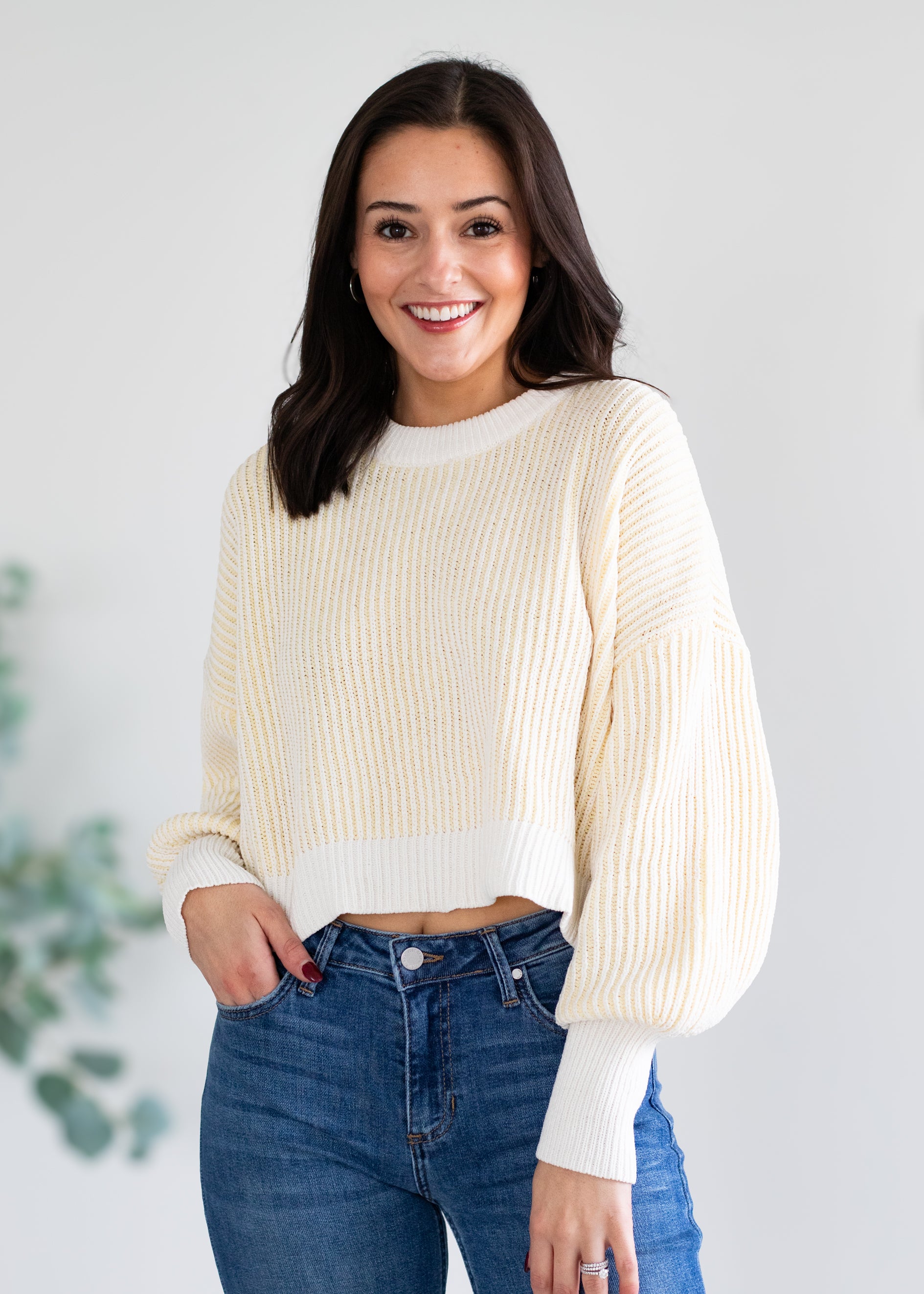 Woman wearing a cream/yellow ribbed sweater and blue jeans against a light background