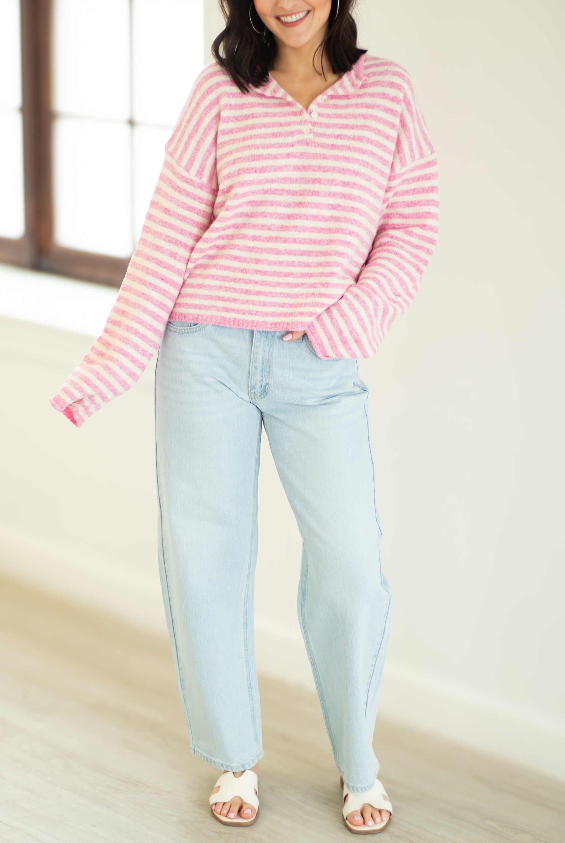 Person wearing a pink and white striped sweater and light blue jeans indoors.