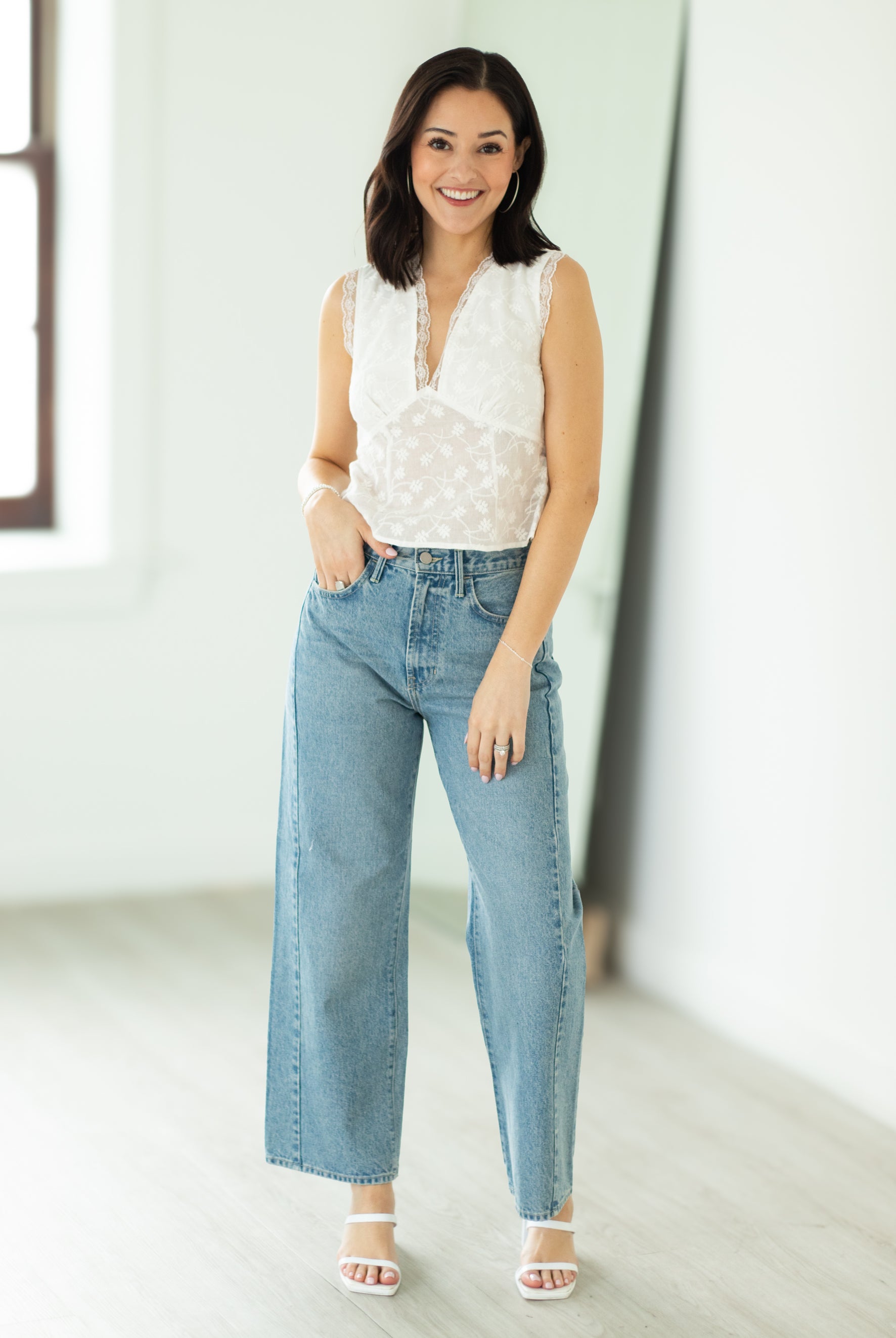 Woman wearing a white blouse and light blue jeans in a bright room.