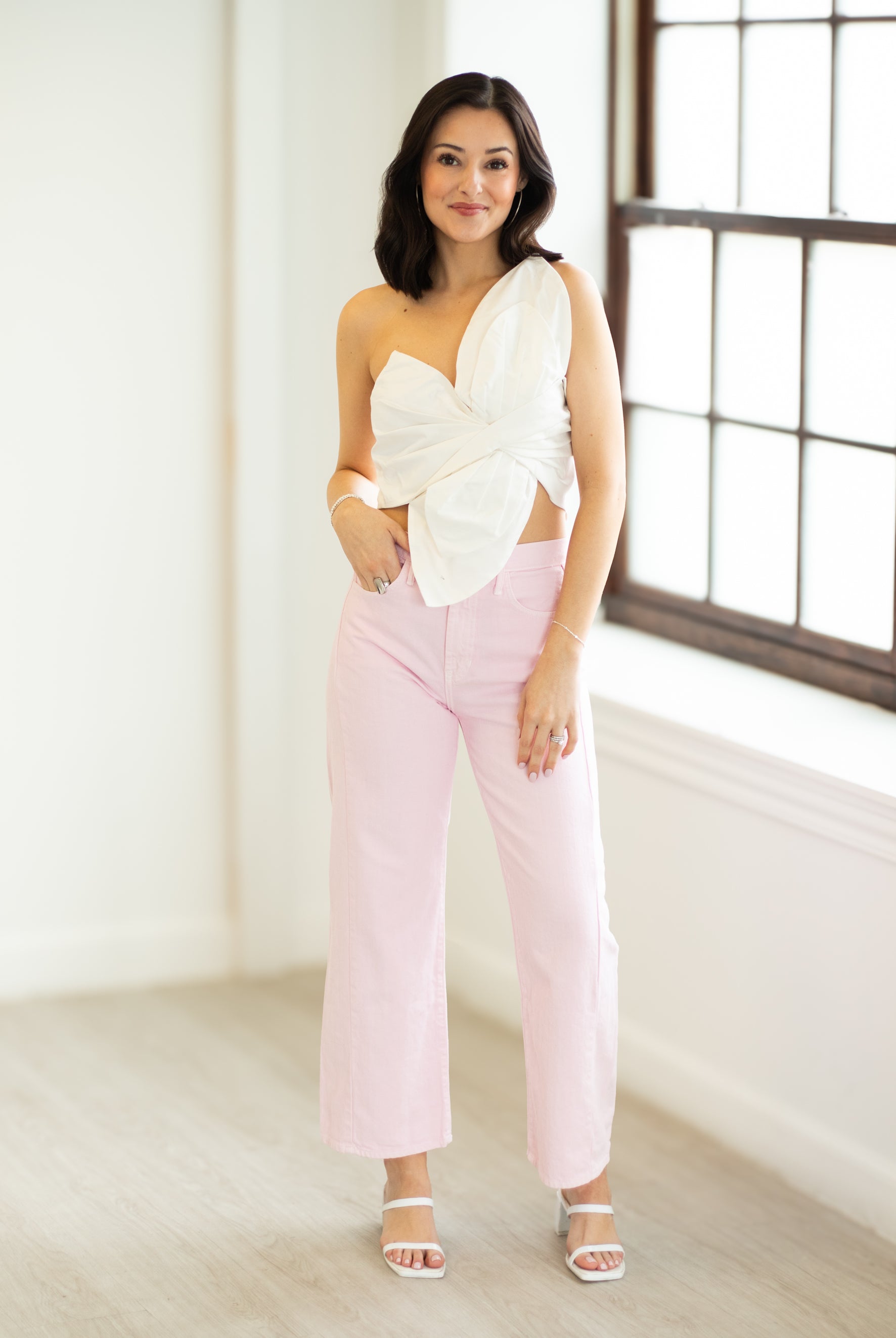 Woman wearing a white top and pink pants in a bright room.