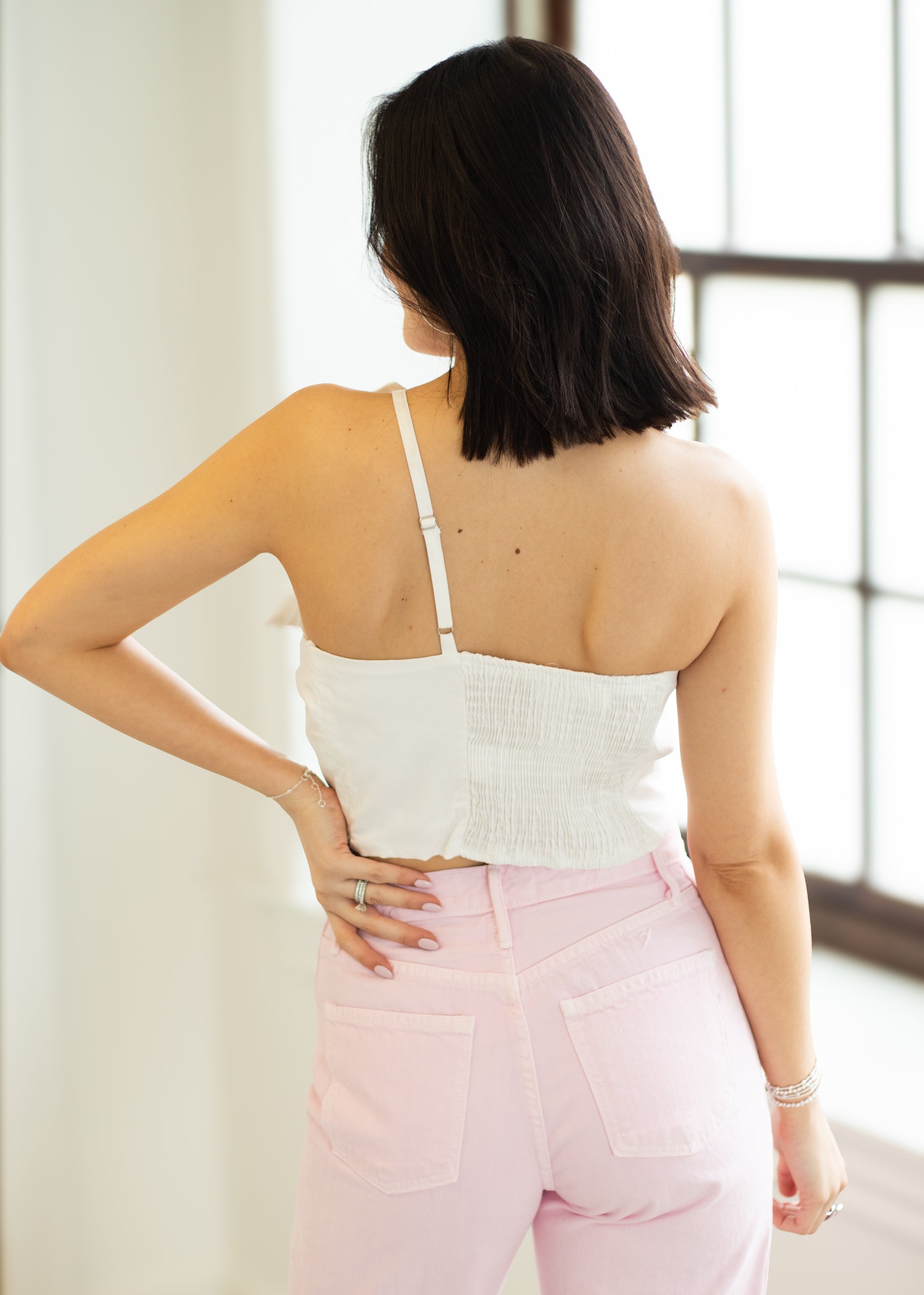 Woman wearing a white top and pink pants in a bright room.
