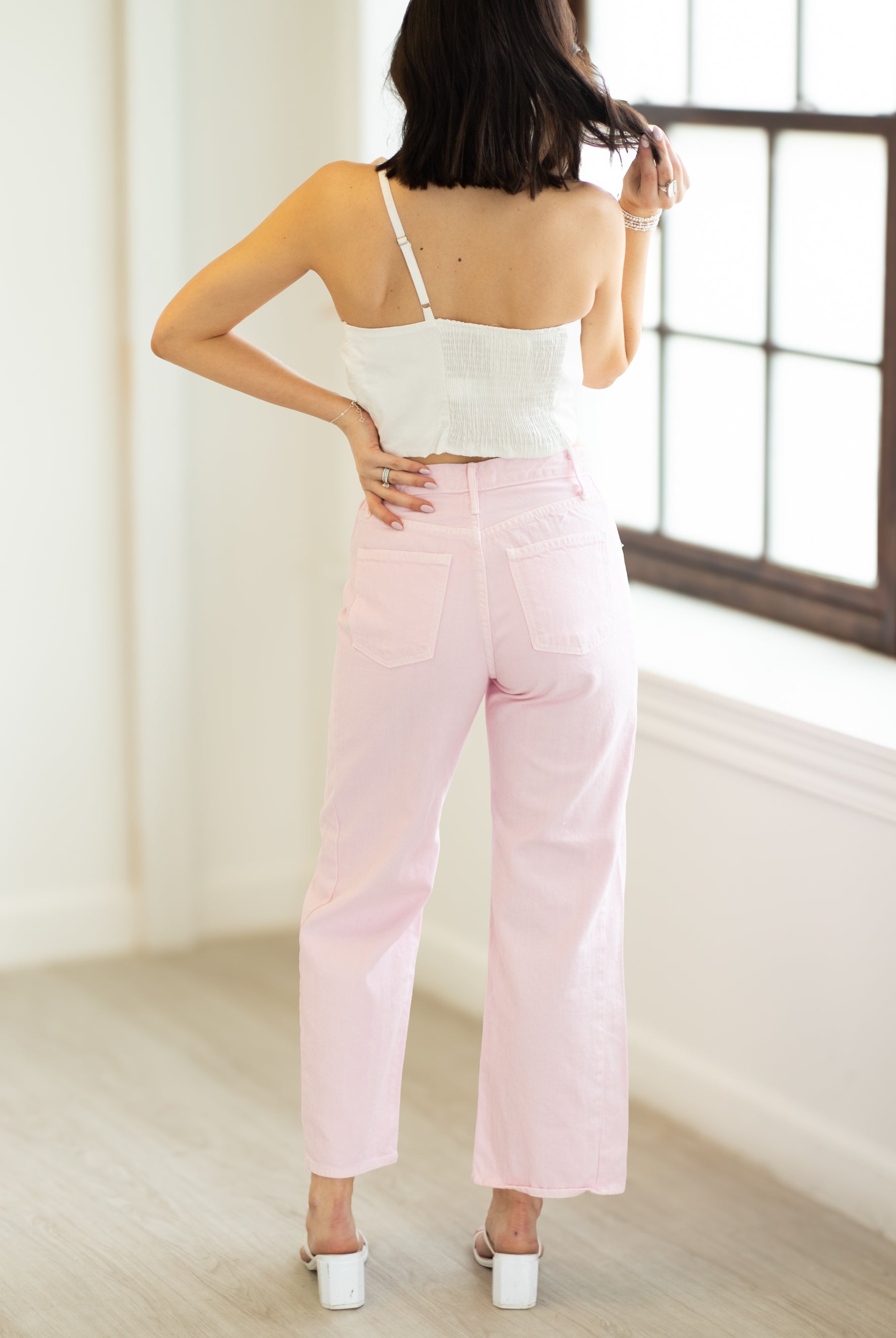 Woman wearing a white top and pink pants in a minimalistic room.