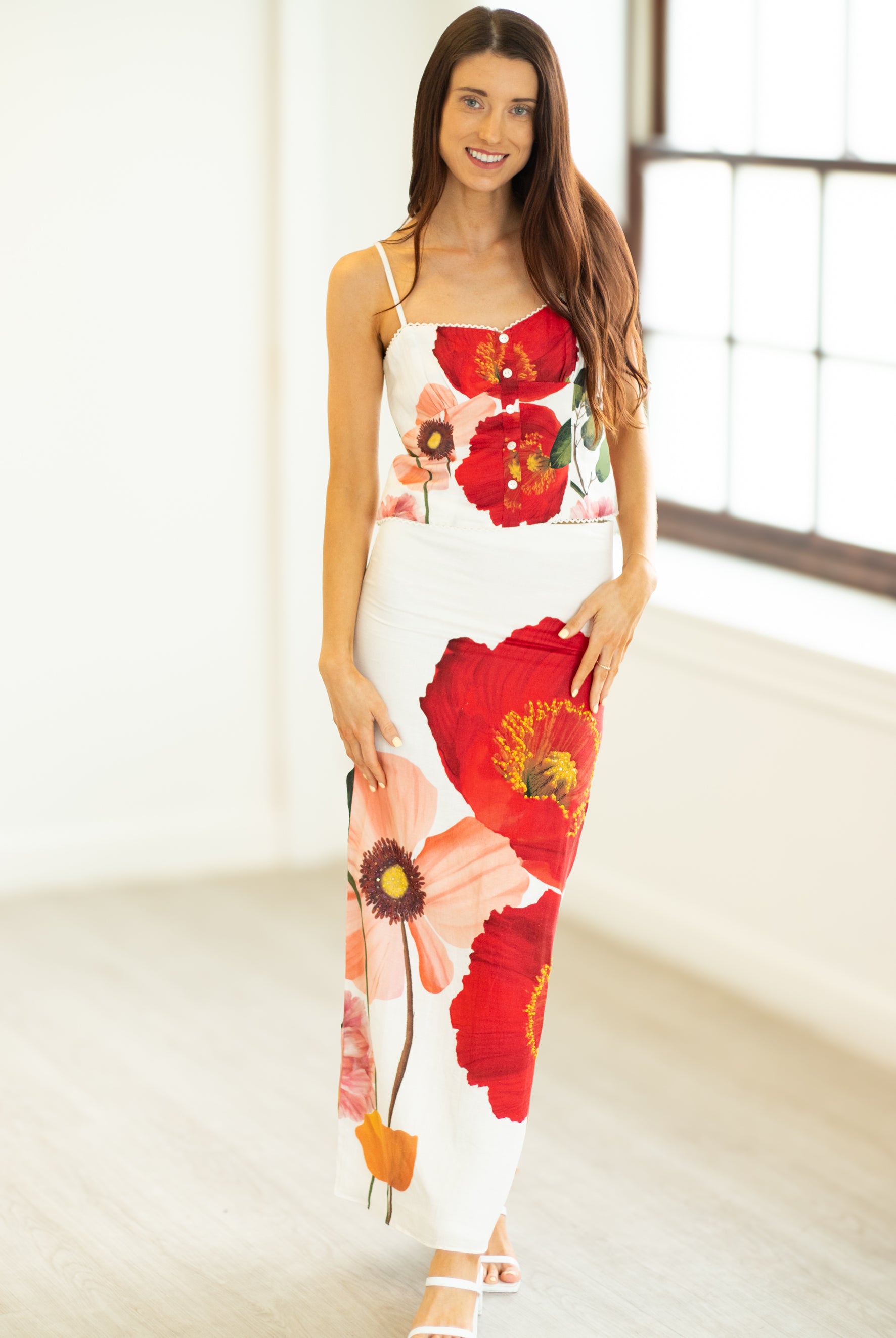 Woman wearing a floral dress with red flowers in a bright room.