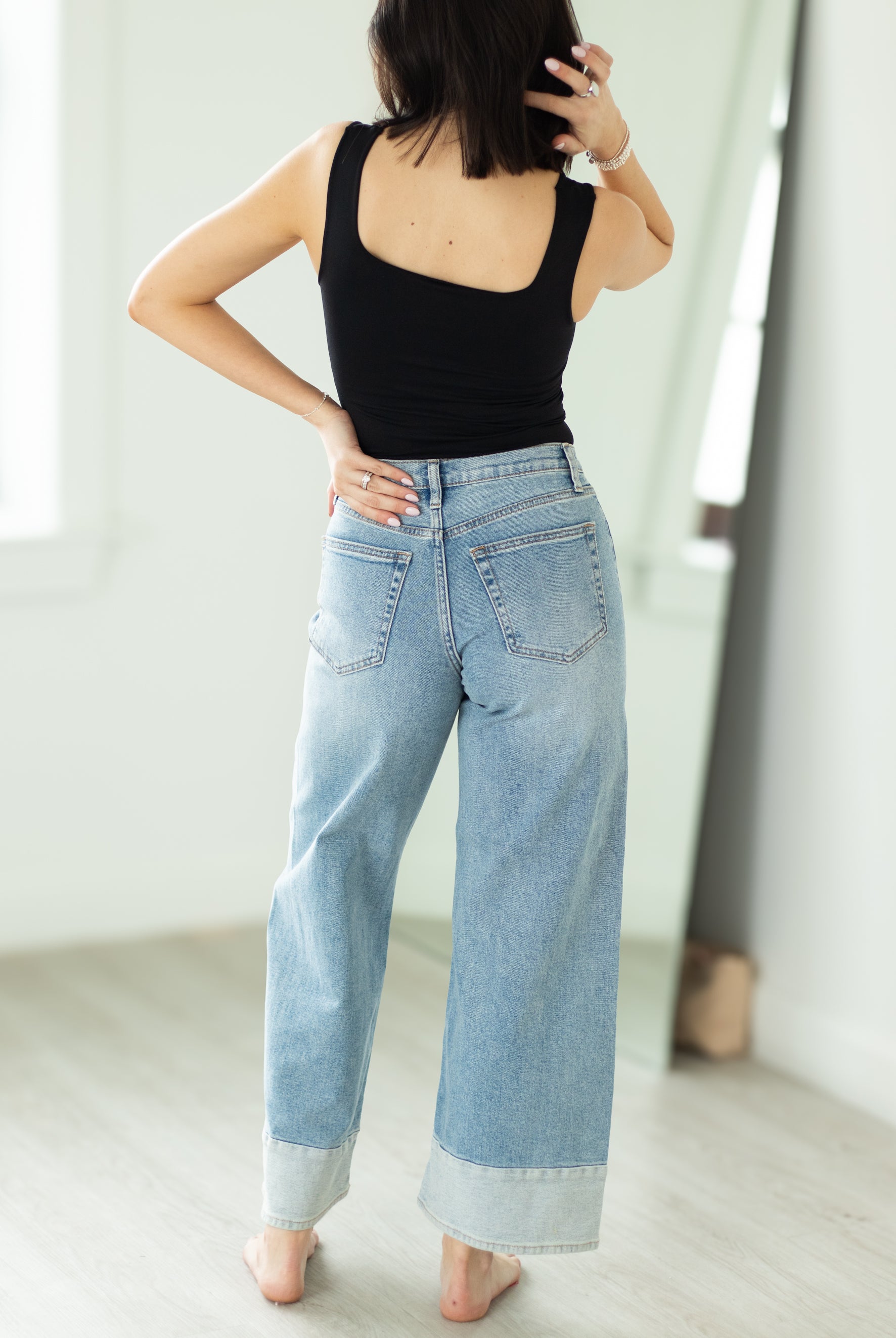 Person wearing a black tank top and light blue jeans indoors.