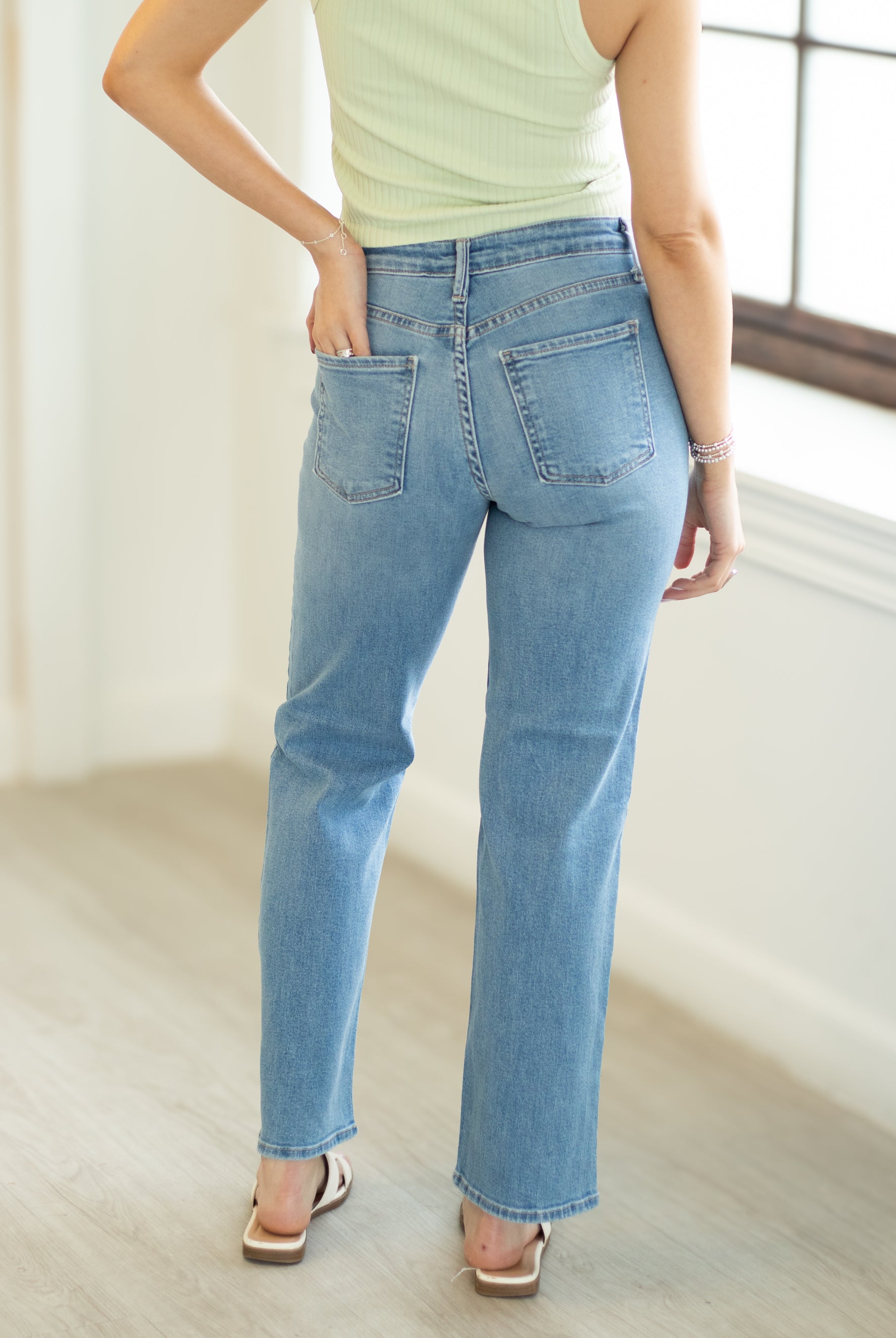 Person wearing light blue jeans and a light green top in a bright room.