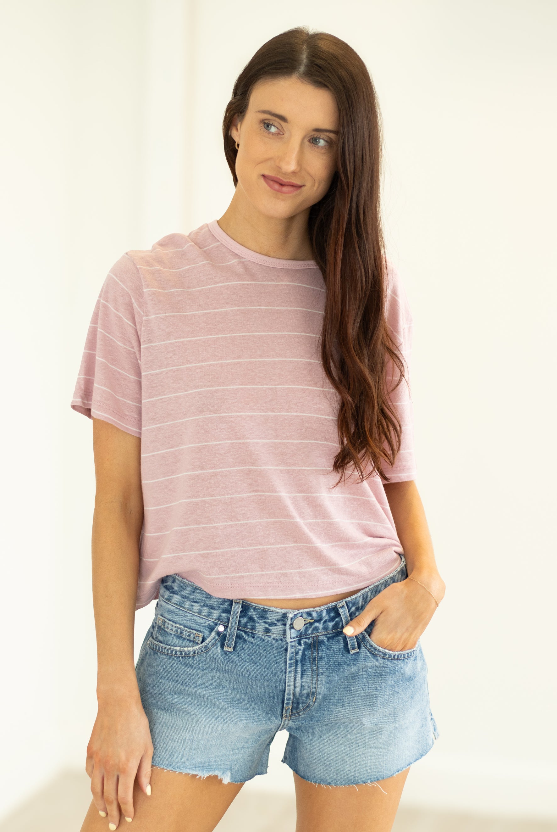 Woman wearing a pink striped t-shirt and denim shorts against a white background