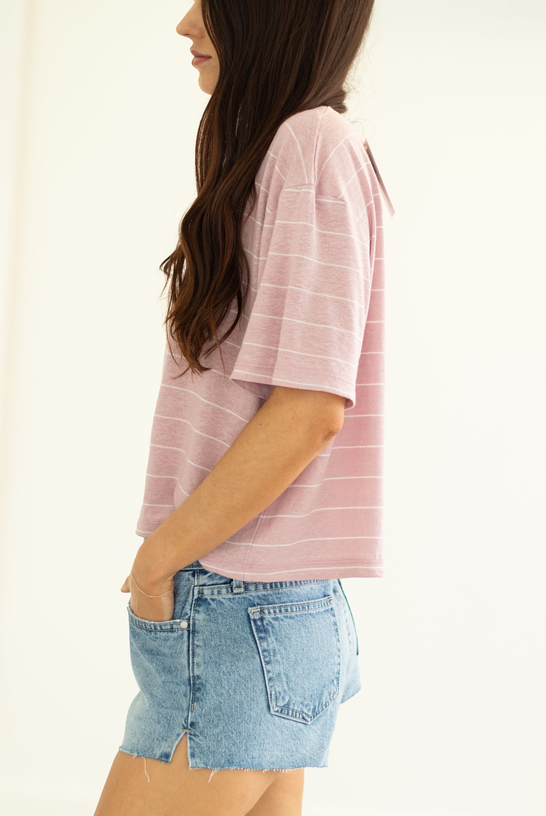 Woman wearing a pink striped shirt and denim shorts on a plain background