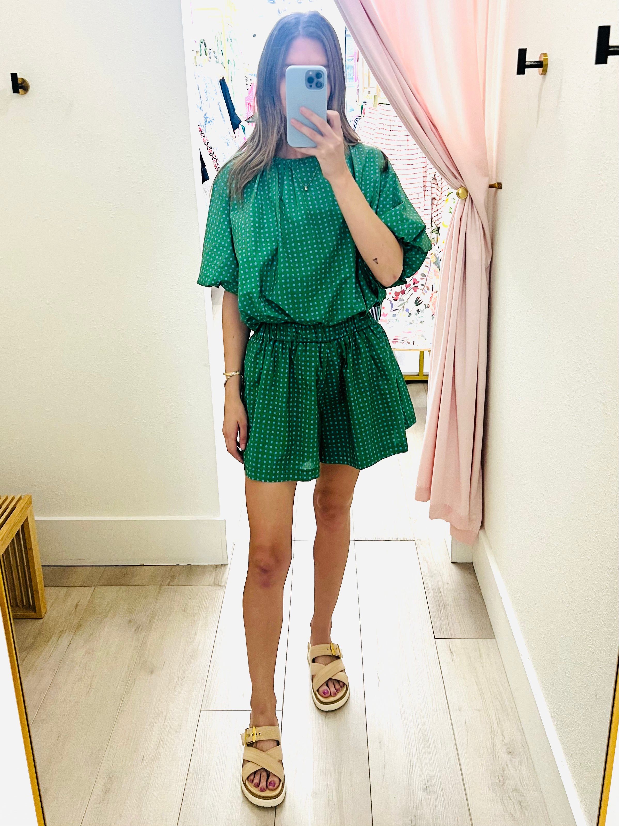 Person wearing a green polka dot outfit taking a mirror selfie.