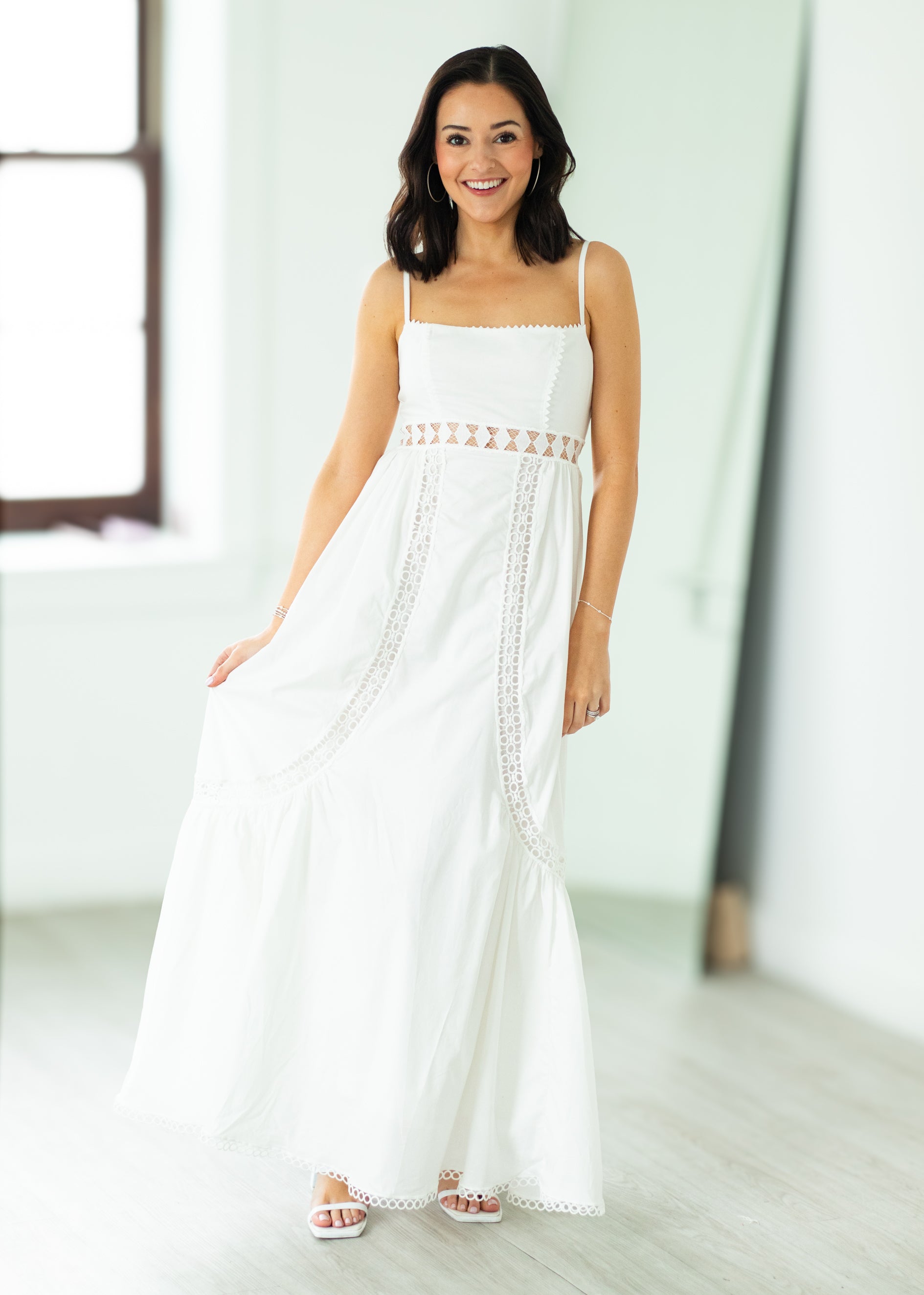 Woman wearing a white dress with lace details in a bright room.