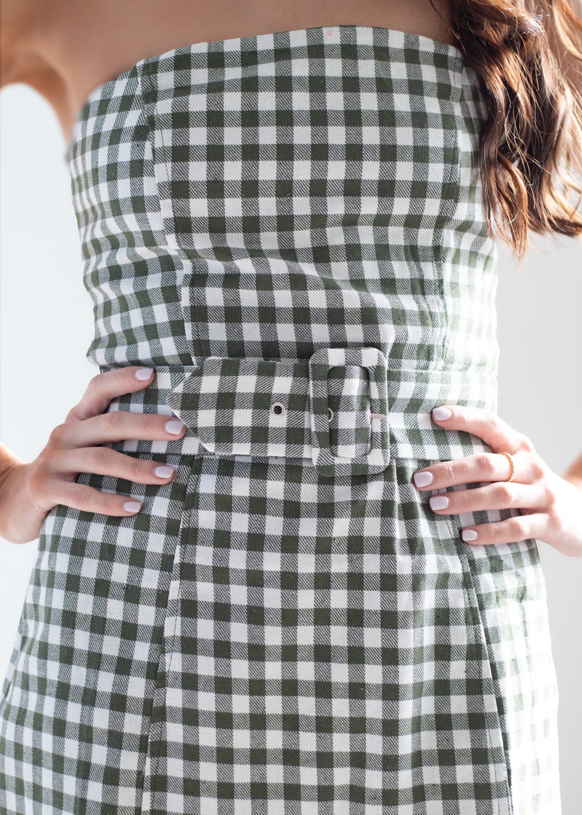 A close-up of a woman wearing a strapless green and white gingham dress with a matching belt and large buckle at the waist.
