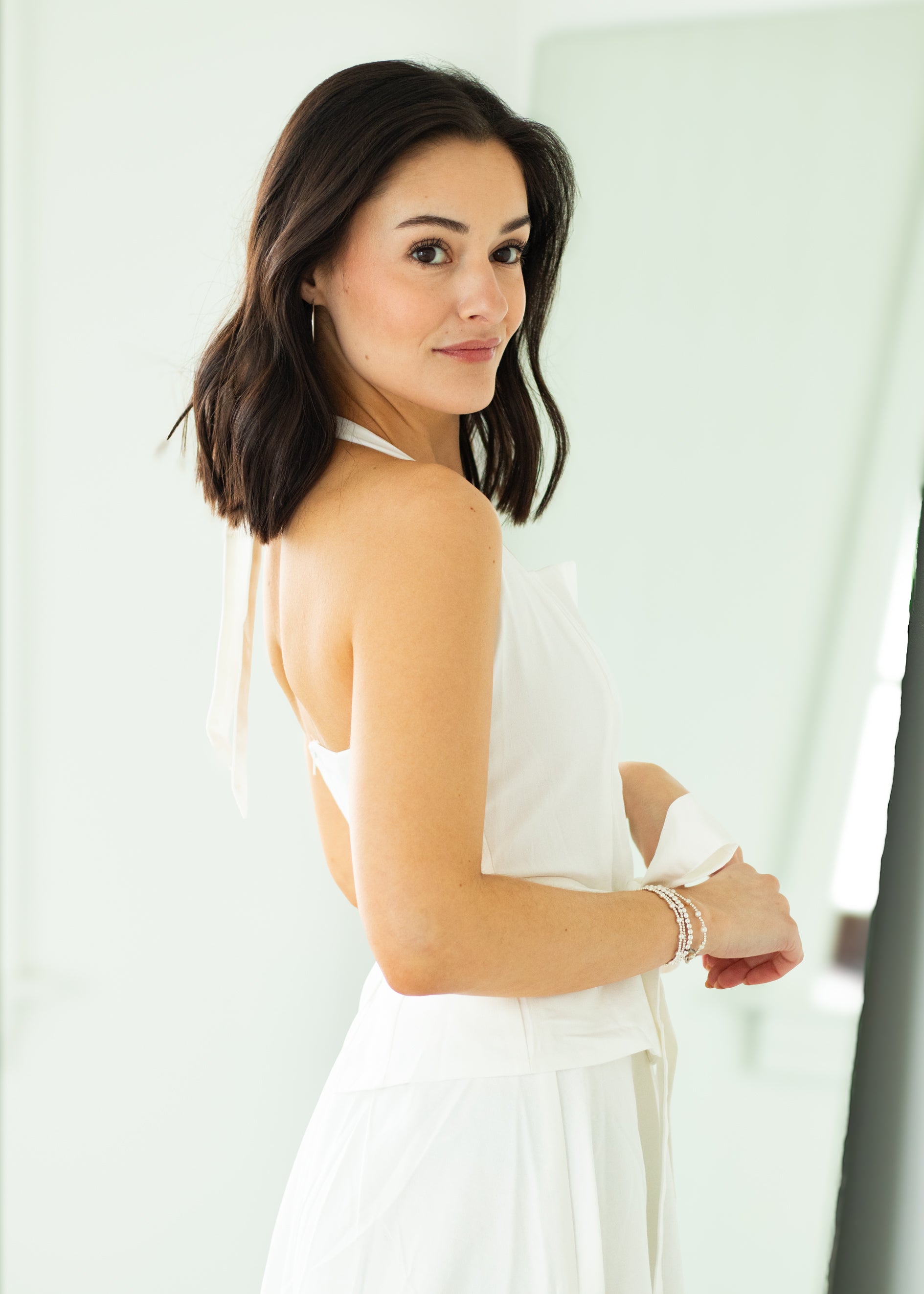 Woman wearing a white halter neck dress with a belt on a beige background