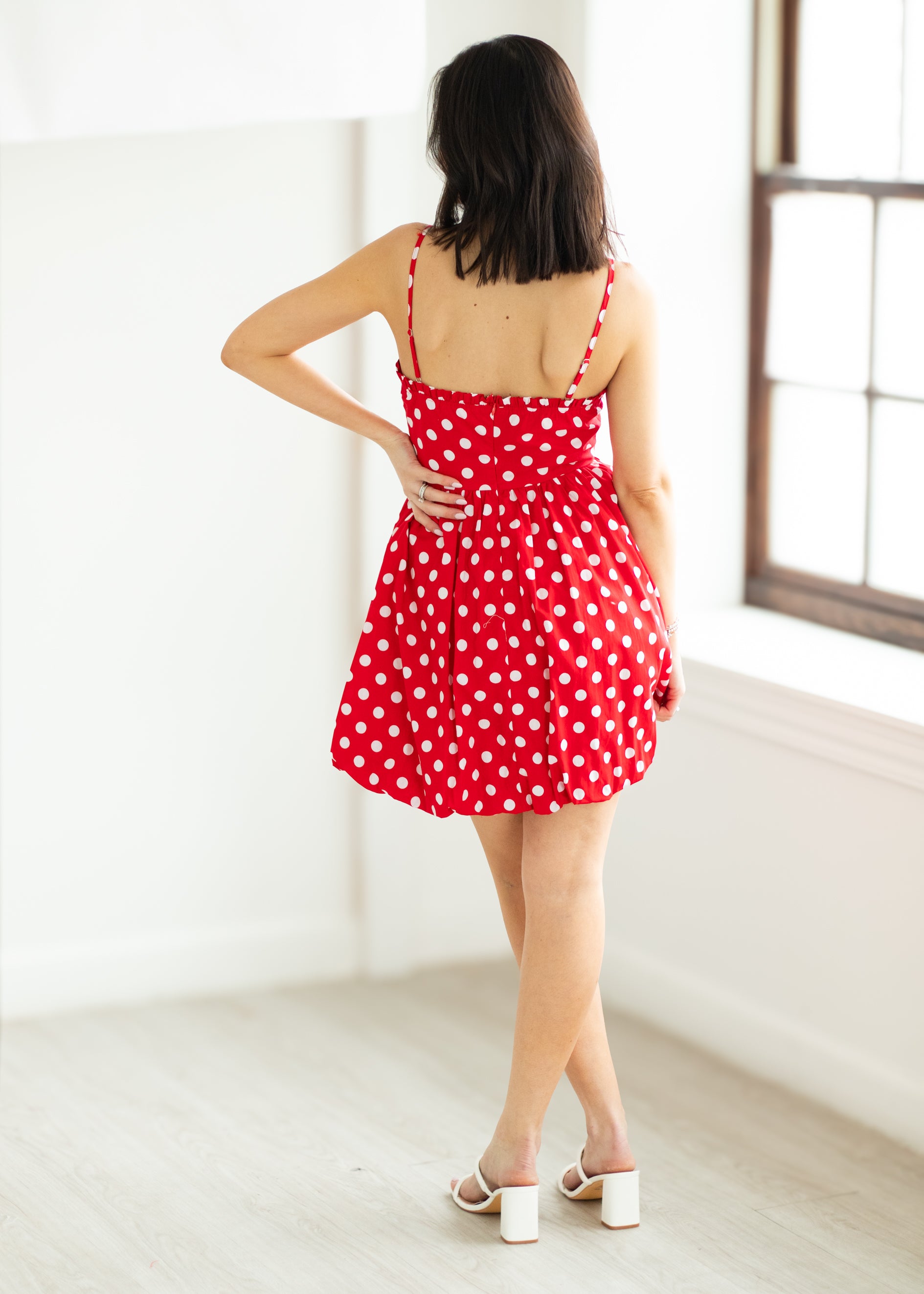 Woman wearing a red polka dot dress with sunglasses on a beige background