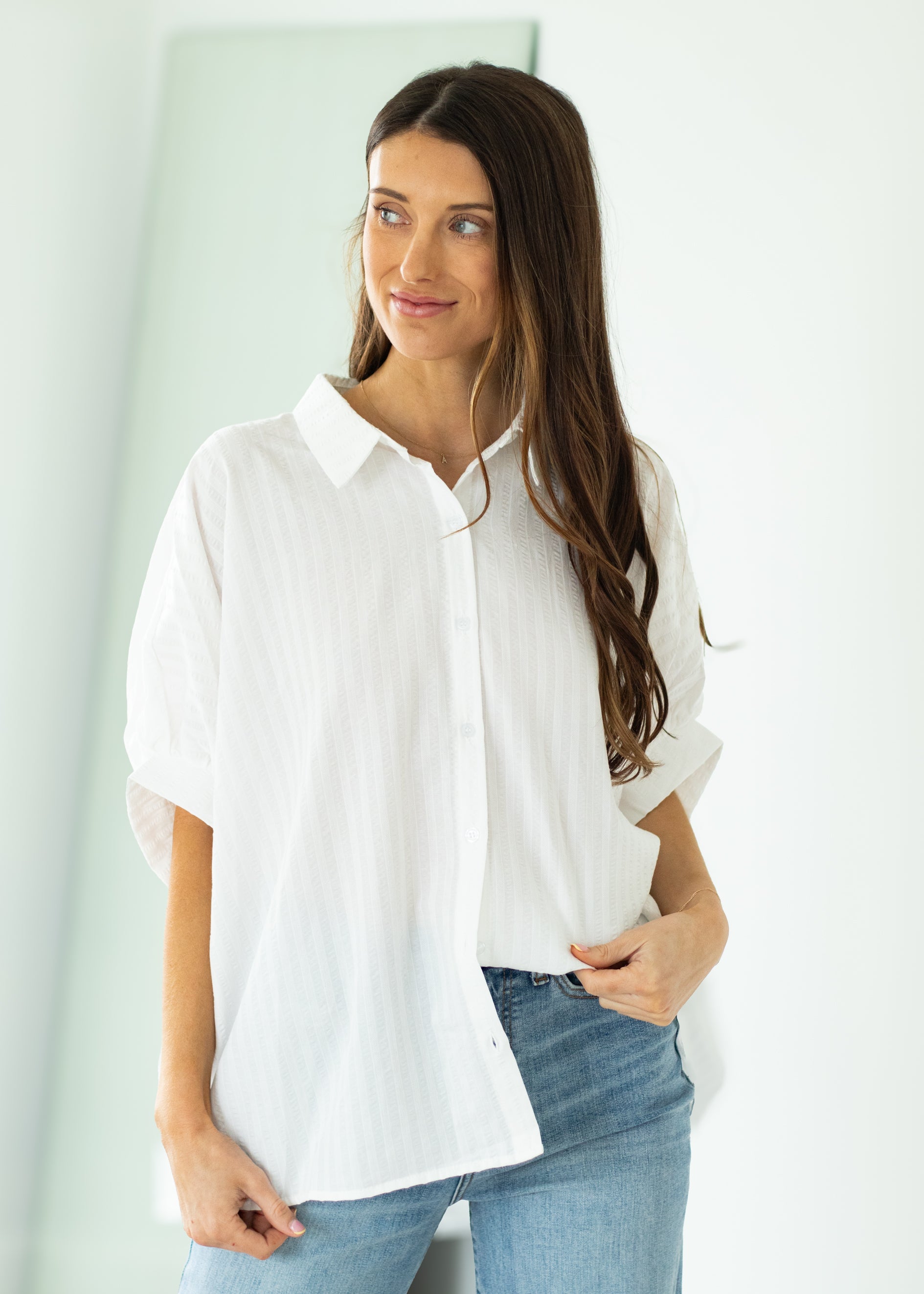 Woman wearing a white oversized shirt and blue jeans against a beige background