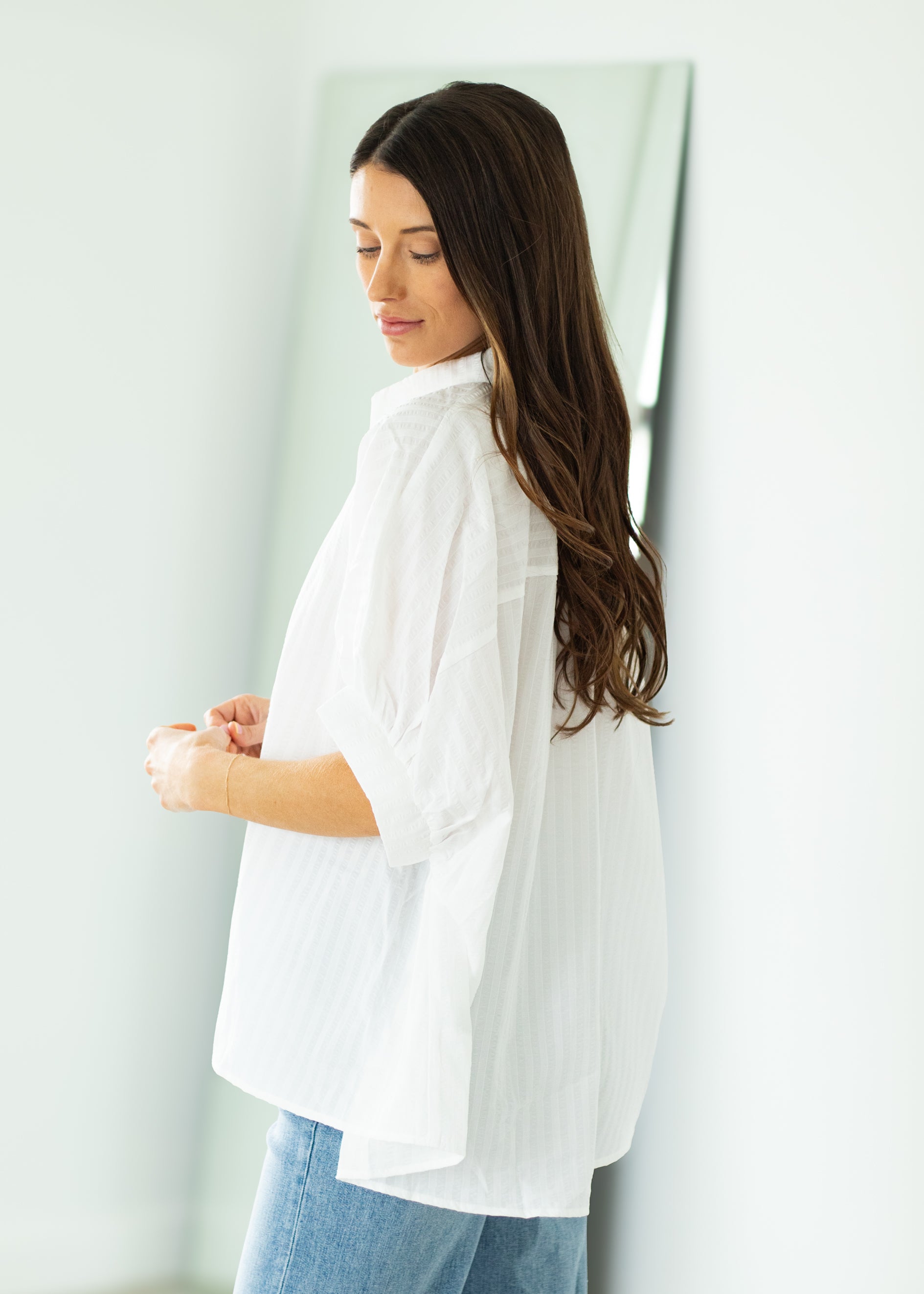 Woman wearing a white oversized shirt and blue jeans against a beige background