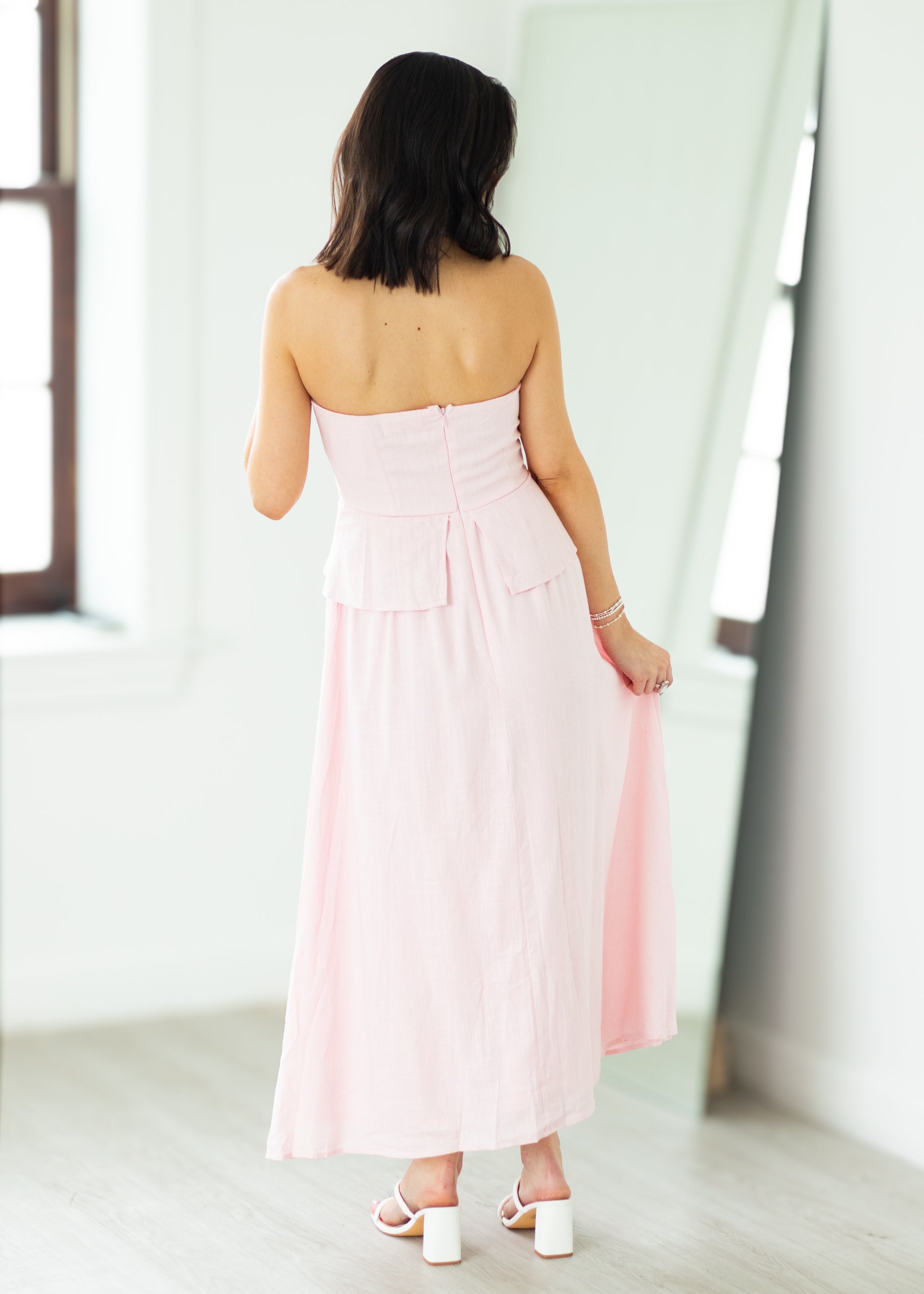 Woman wearing a pink strapless dress with a peplum top on a beige background