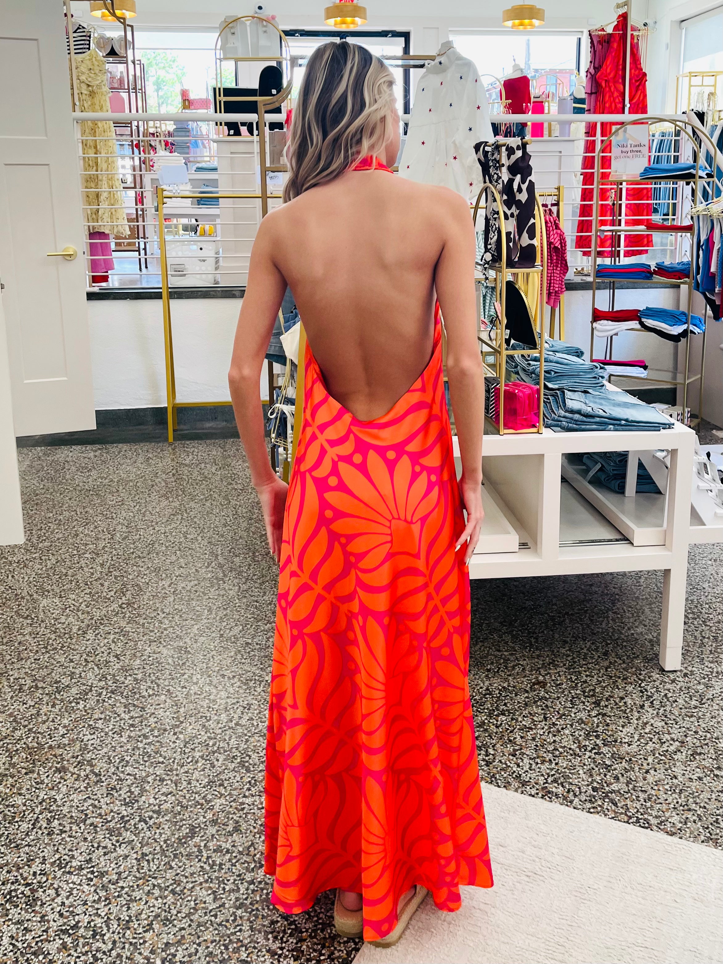 Woman wearing a bright orange dress with a sunflower pattern in a store setting.