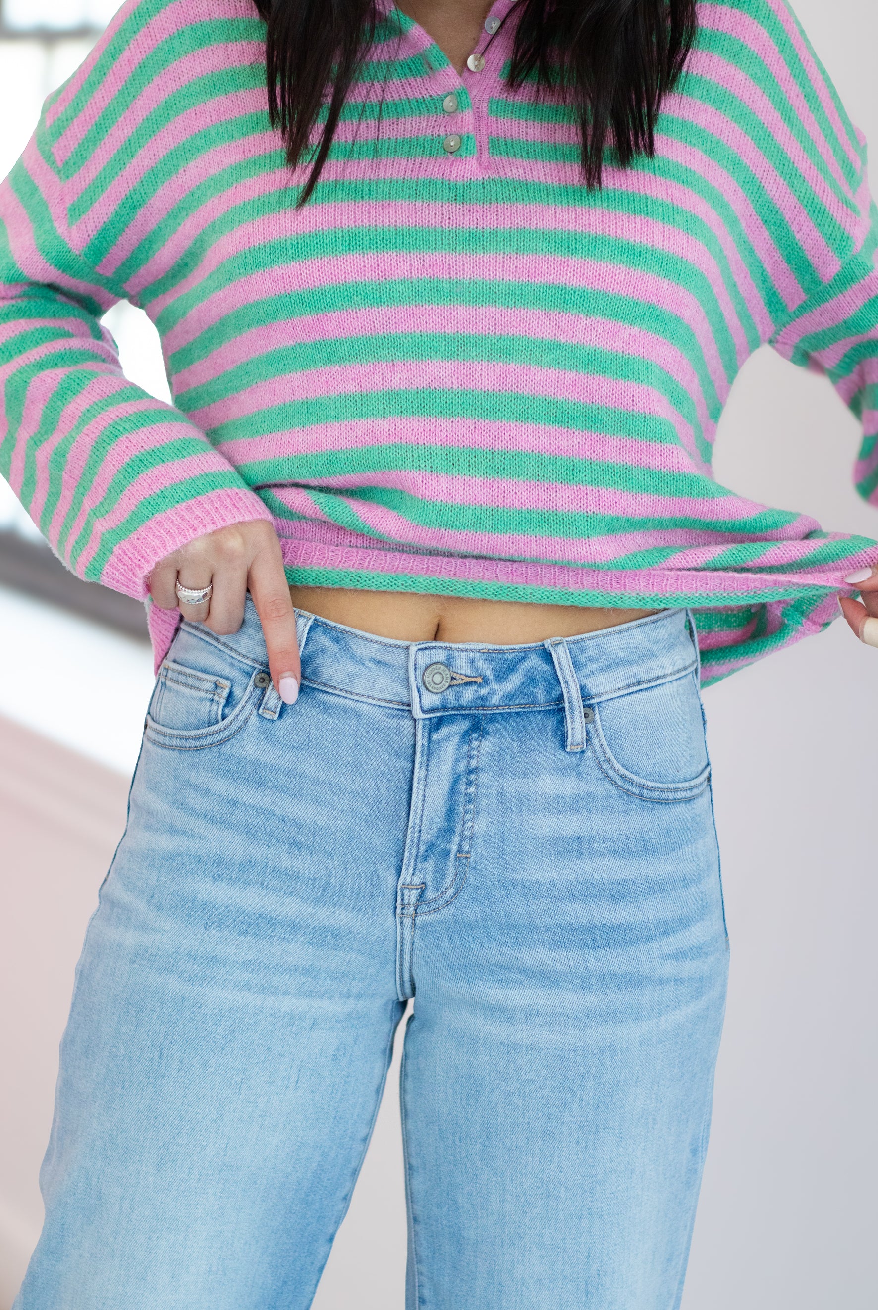 Person wearing a pink and green striped sweater and light blue jeans.