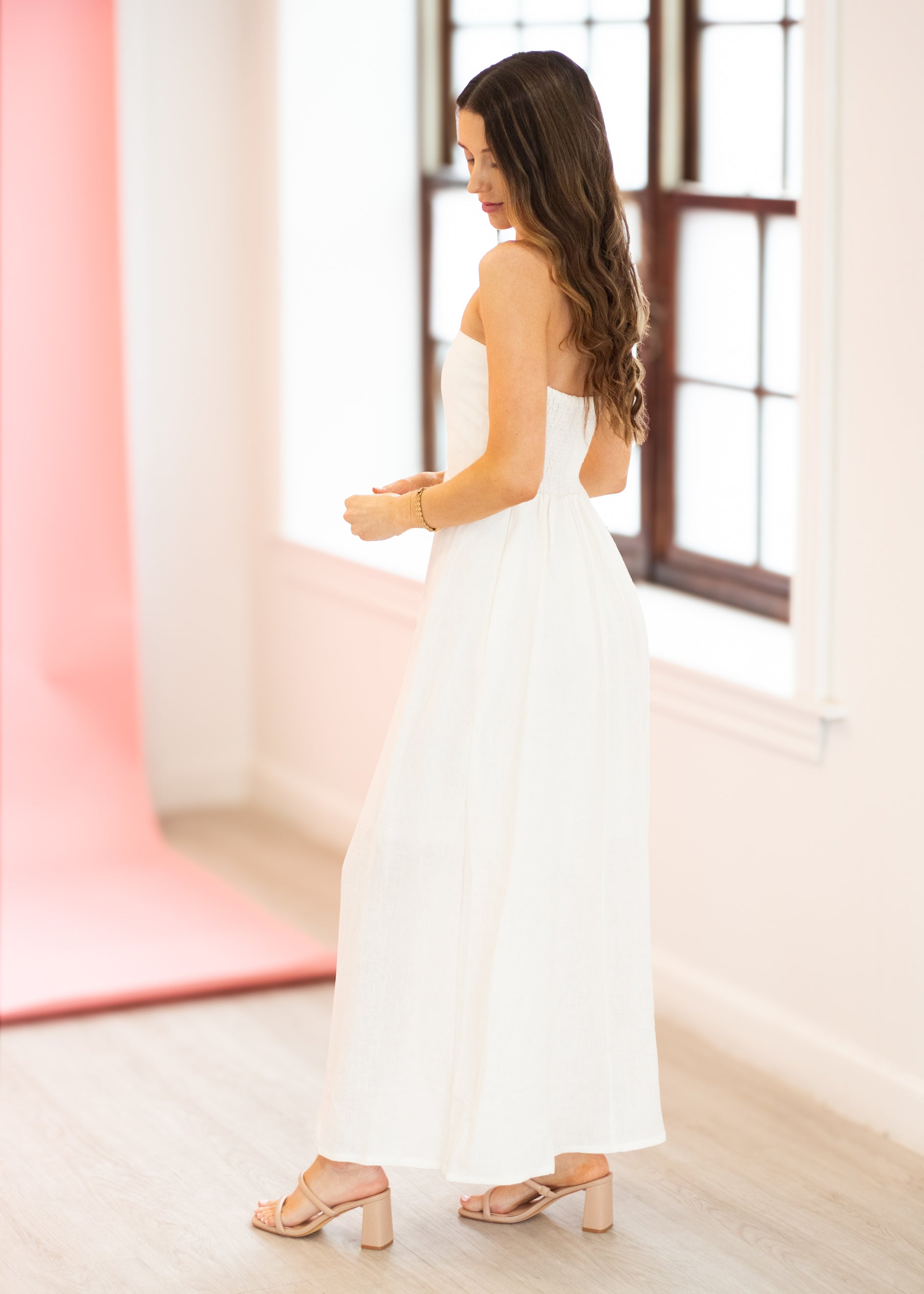 Woman in a white dress standing in a bright room with large windows.