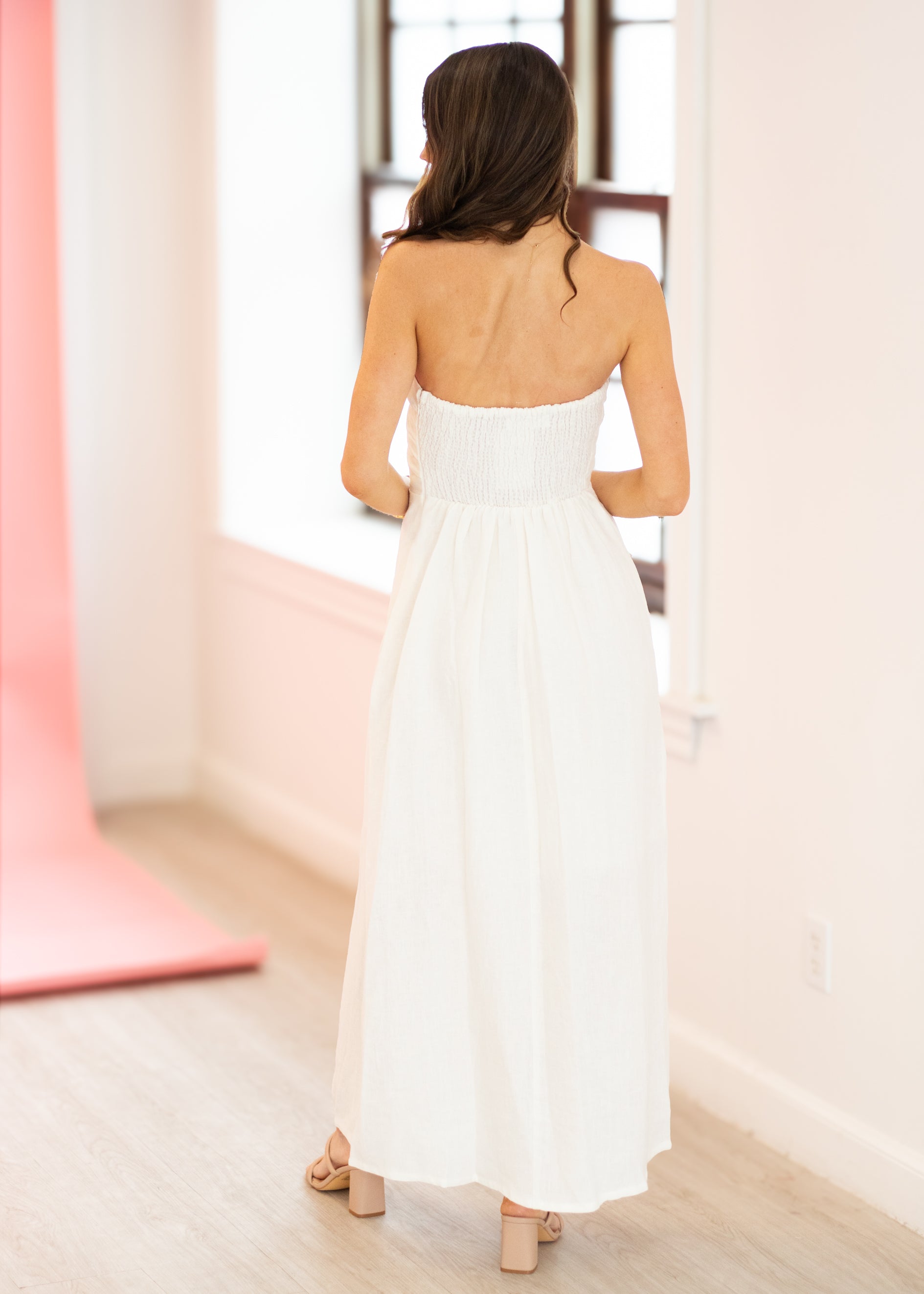 Woman in a white strapless dress standing in a minimalistic room with pink accents.