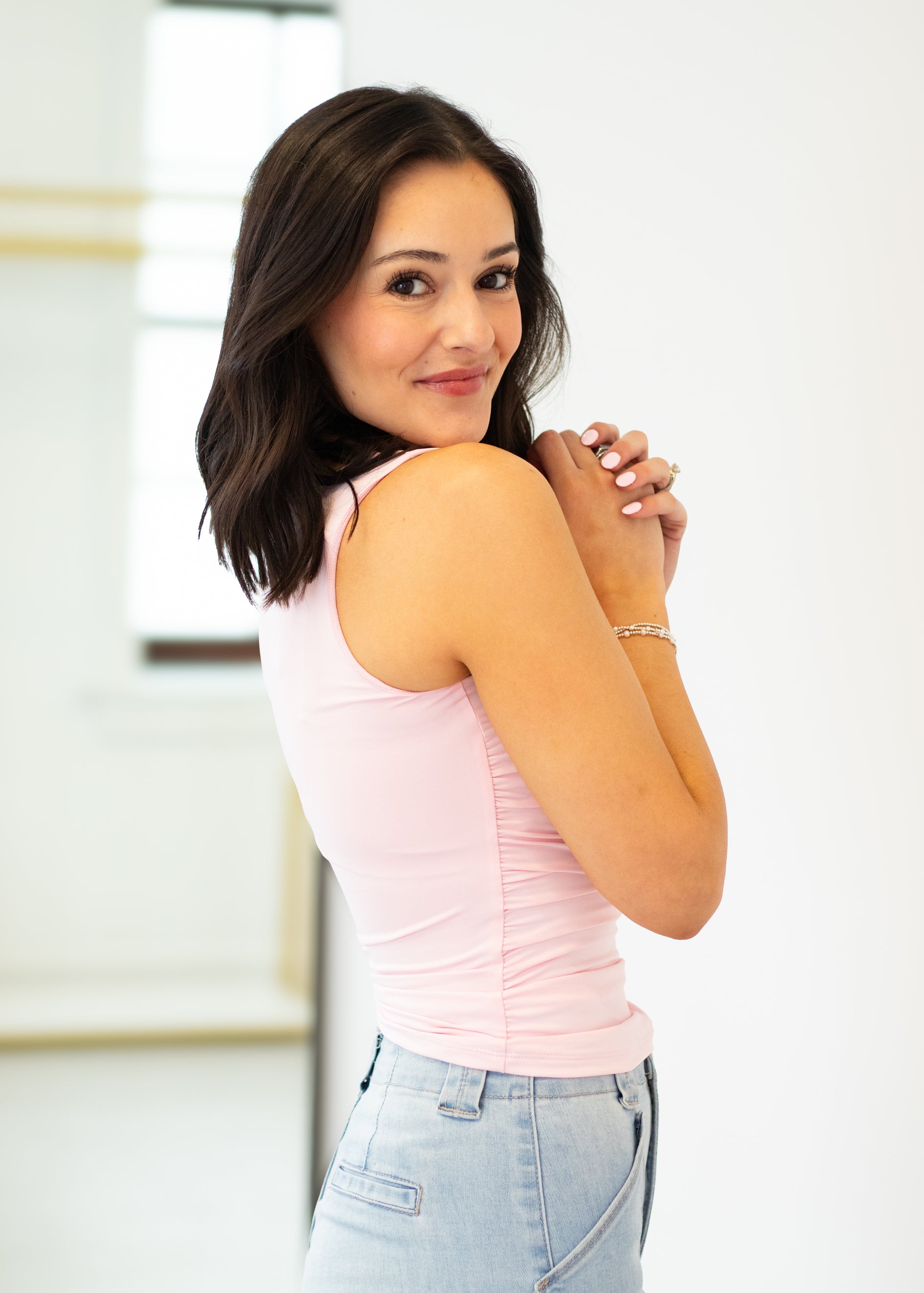 Woman wearing a pink sleeveless top and light blue jeans against a white background