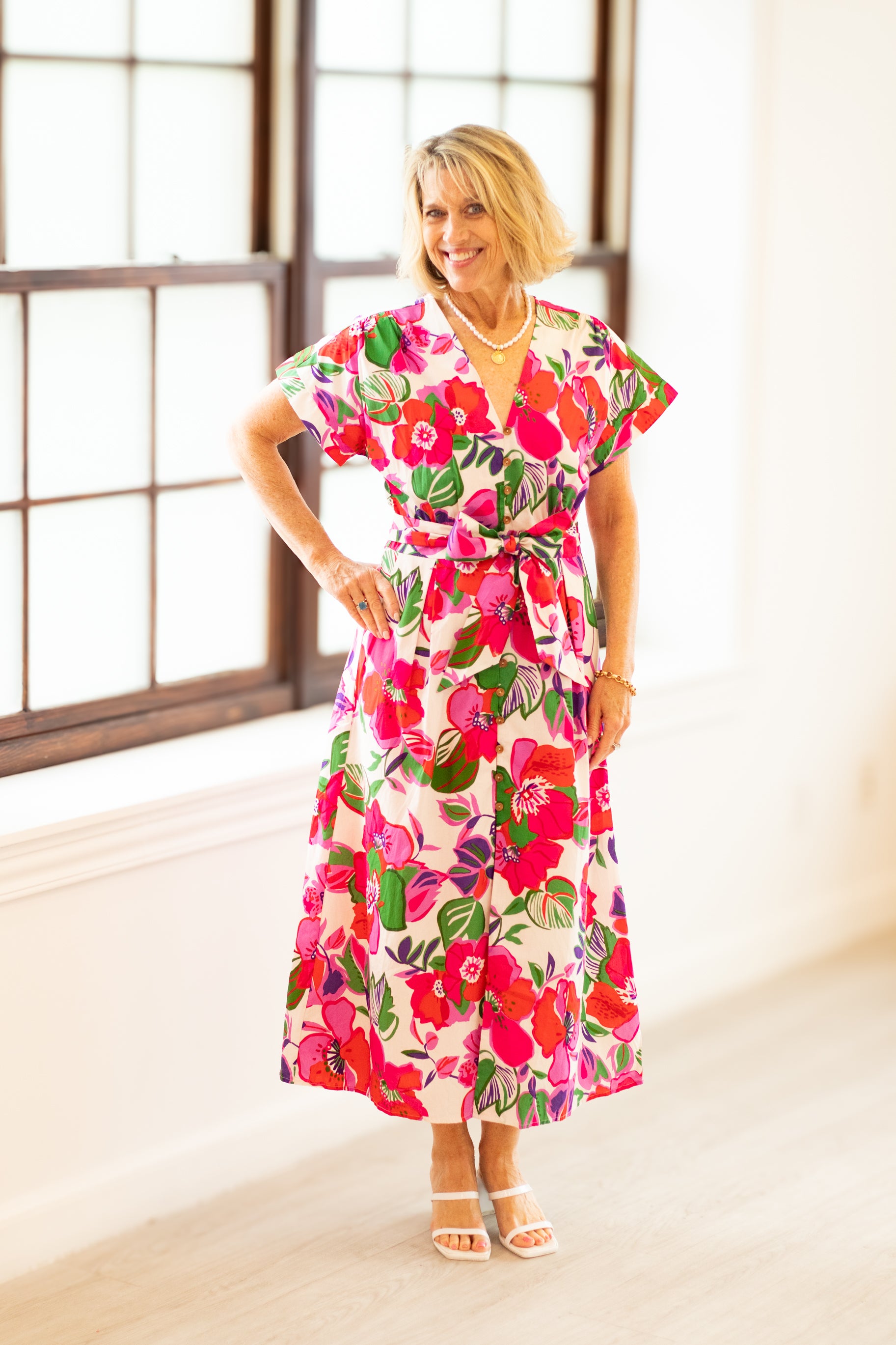 Woman wearing a colorful floral dress in a bright room with large windows.