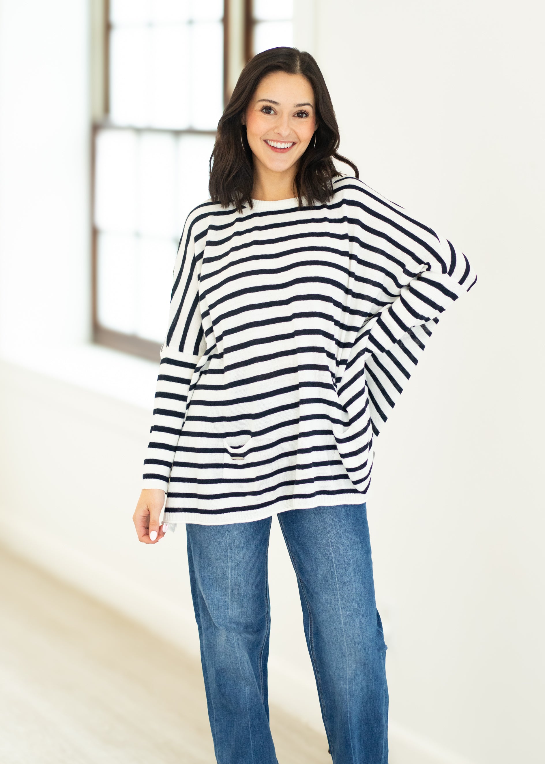 Woman wearing a black and white striped sweater and blue jeans indoors.