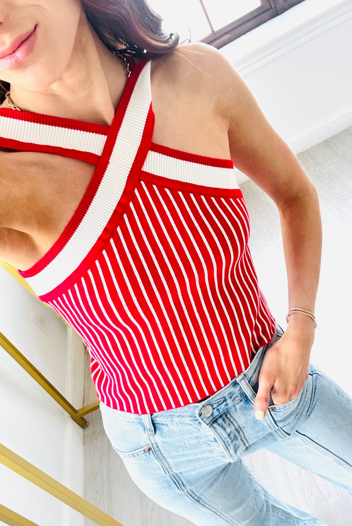 Woman wearing a red and white striped tank top and light blue jeans indoors.