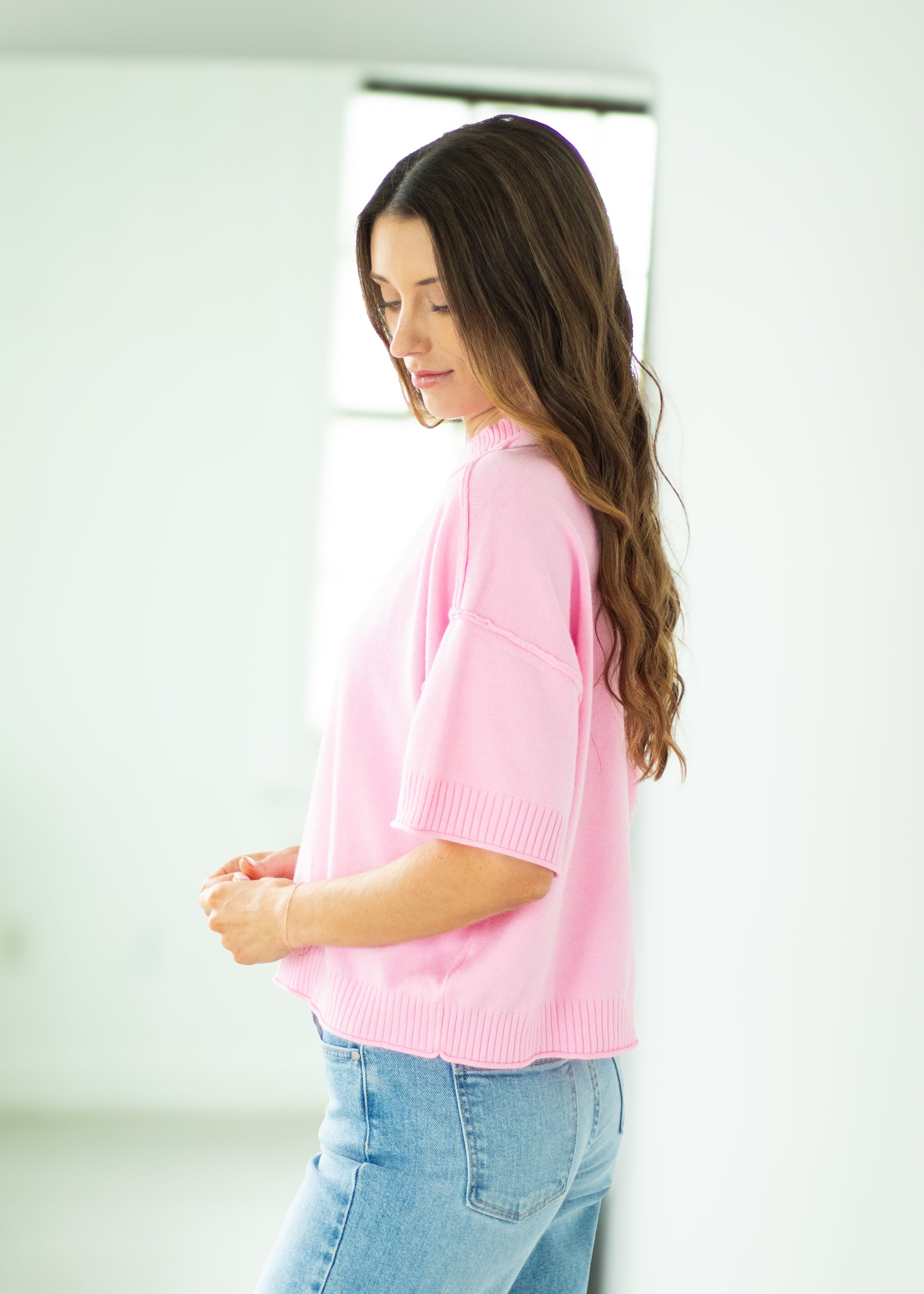 Woman wearing a pink sweater and blue jeans against a white background