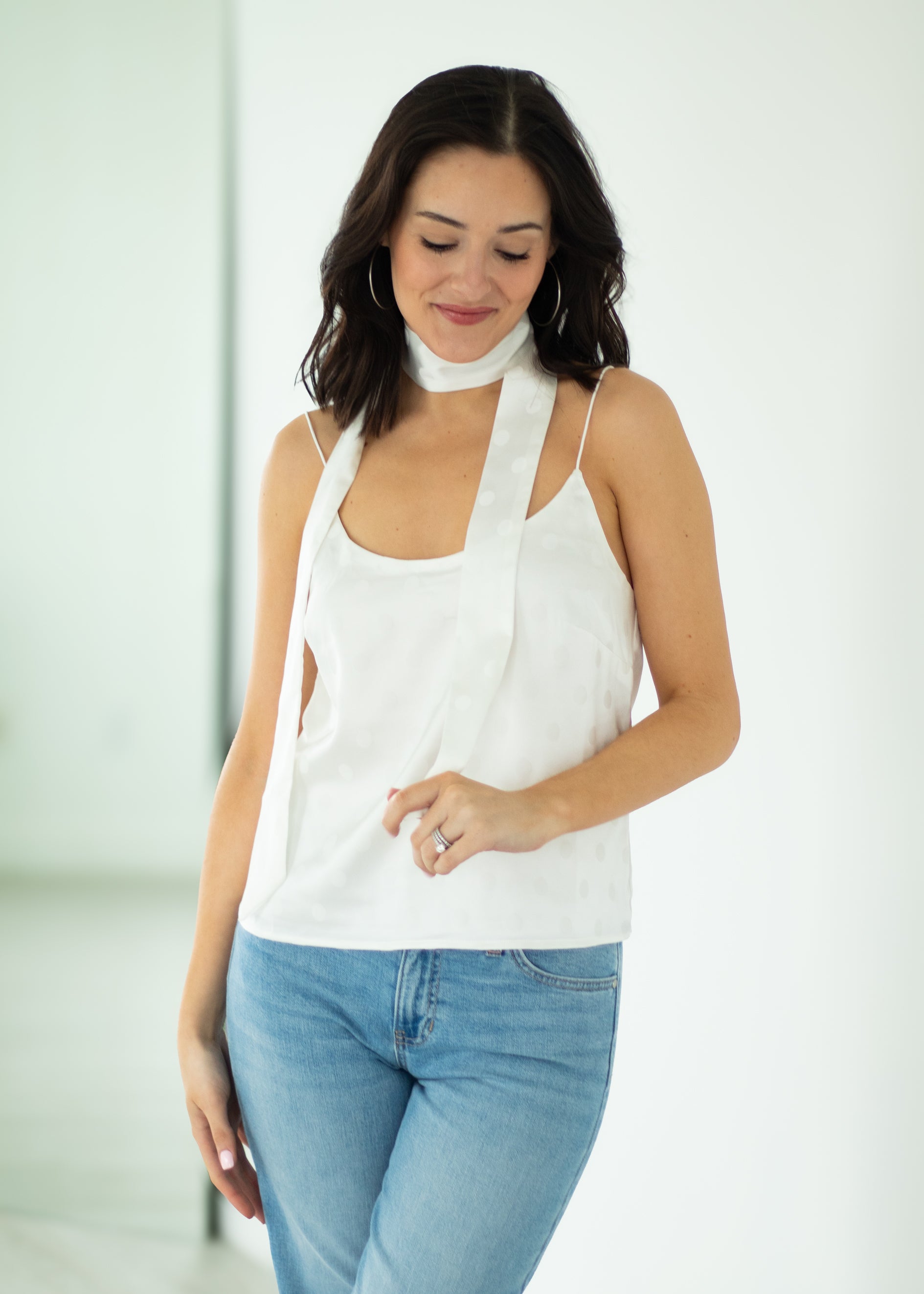Woman wearing a white tank top and blue jeans with a plain background