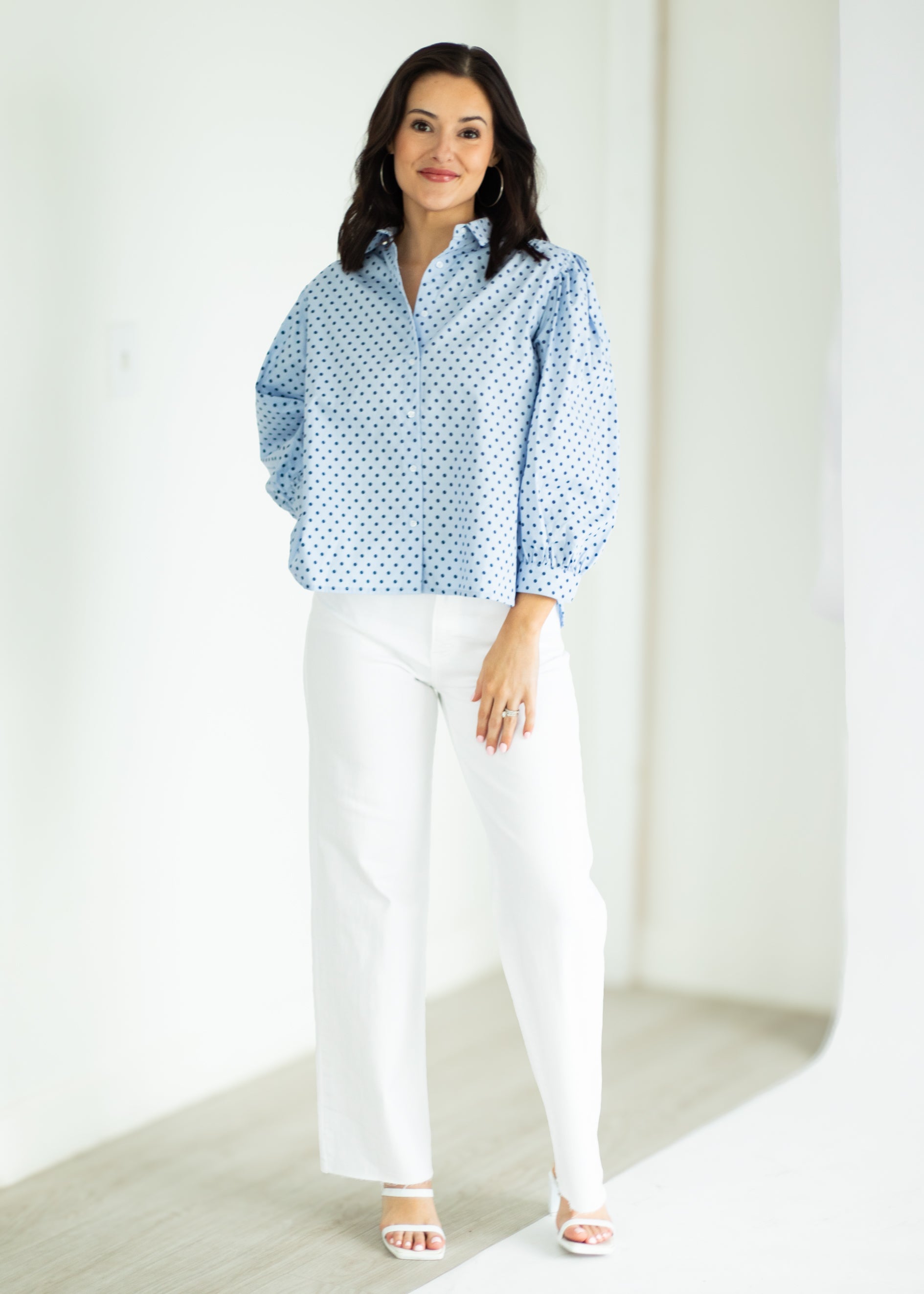 Woman wearing a blue patterned blouse and white pants against a white background