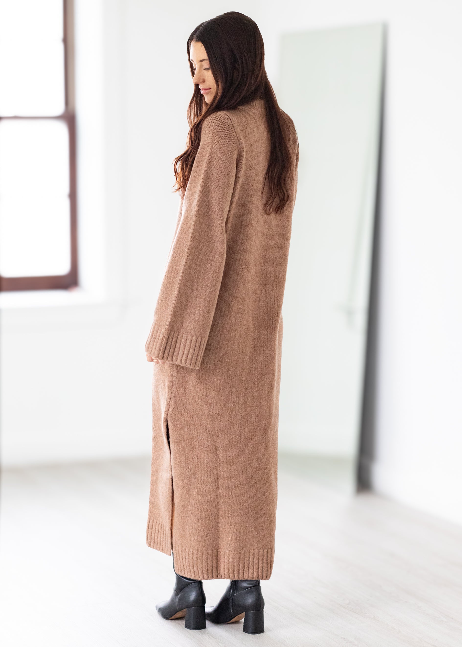 Woman wearing a long beige cardigan in a minimalistic setting
