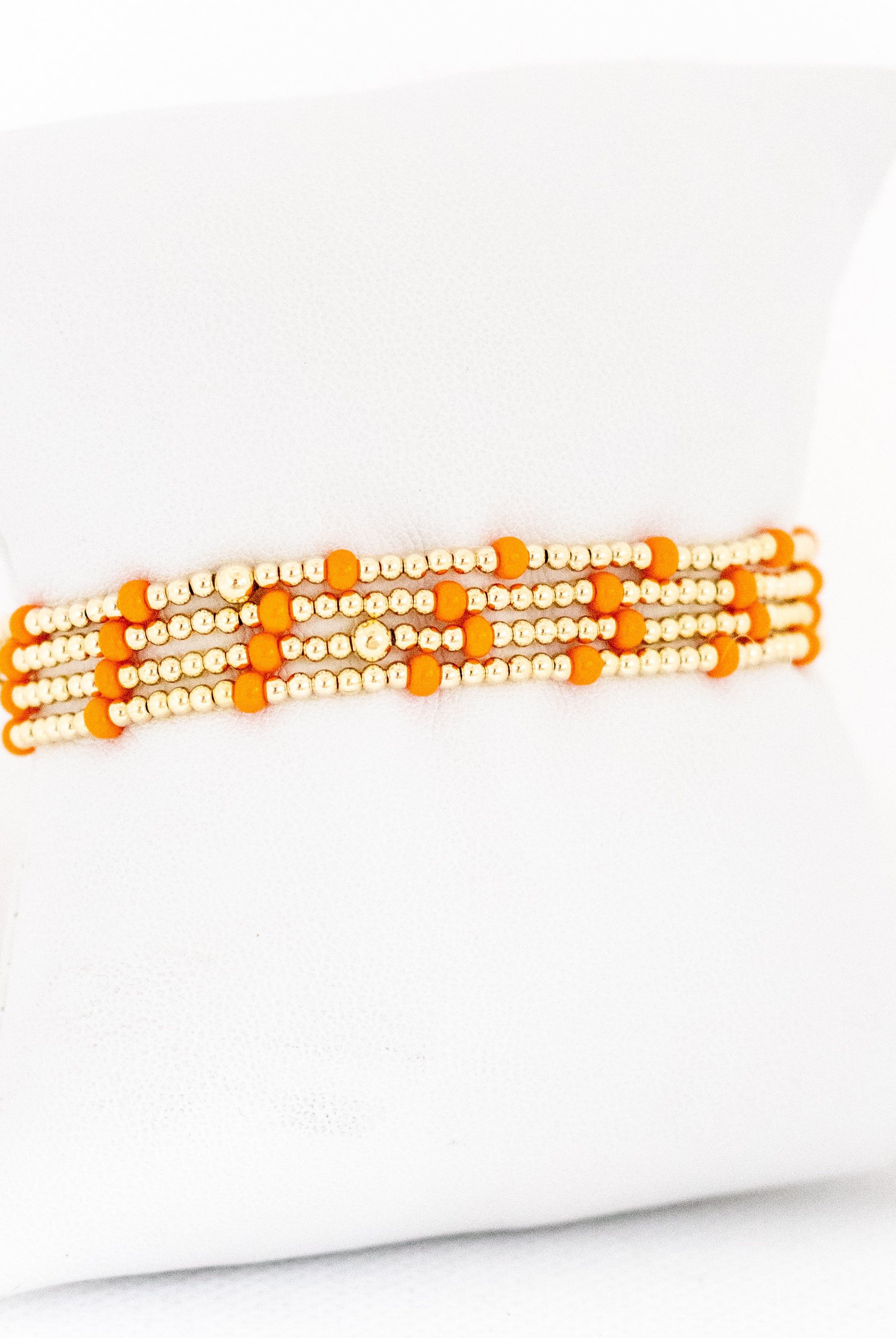 Set of orange and gold beaded bracelets on a white background