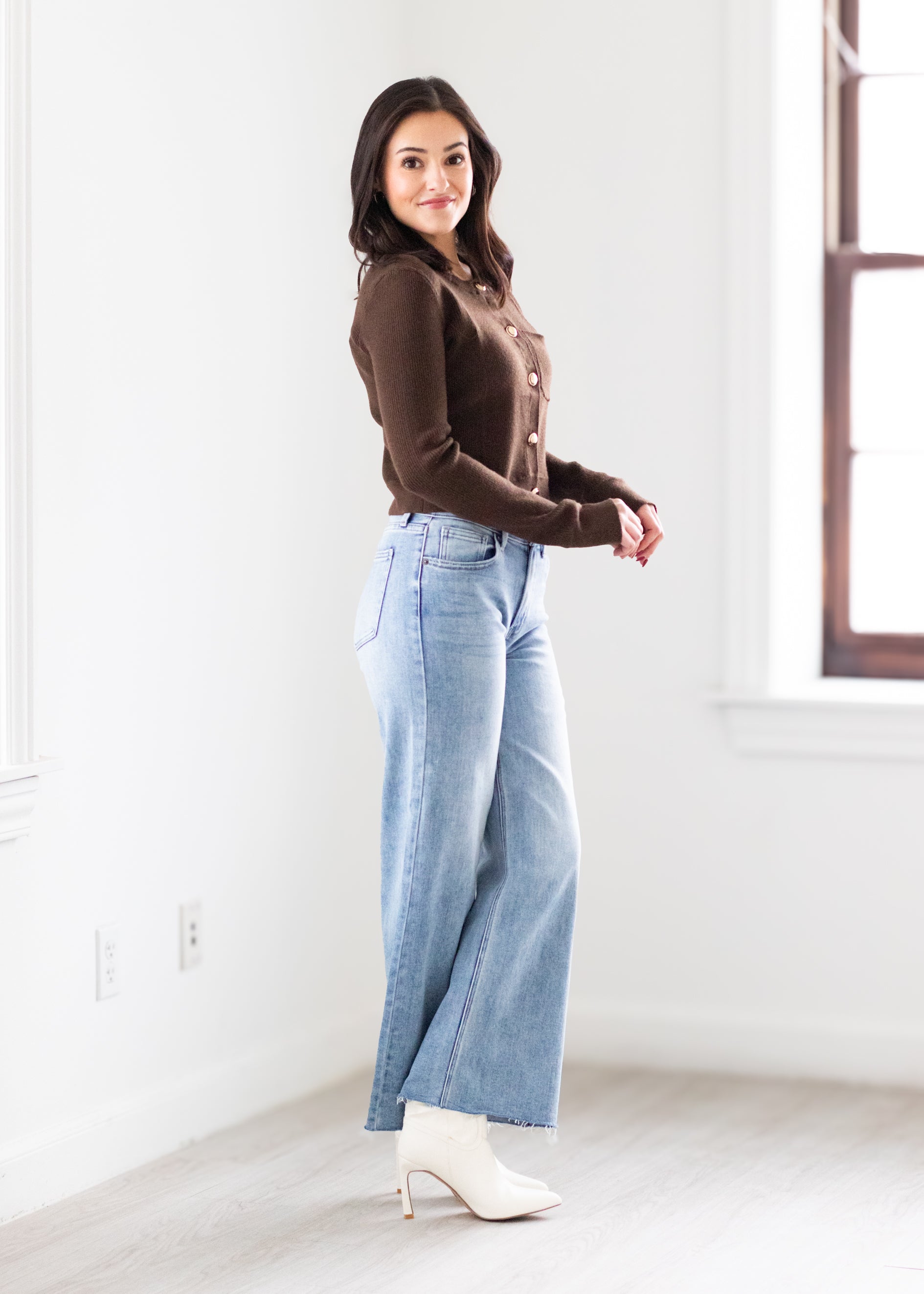 Woman wearing a brown top and blue jeans standing in a bright room.