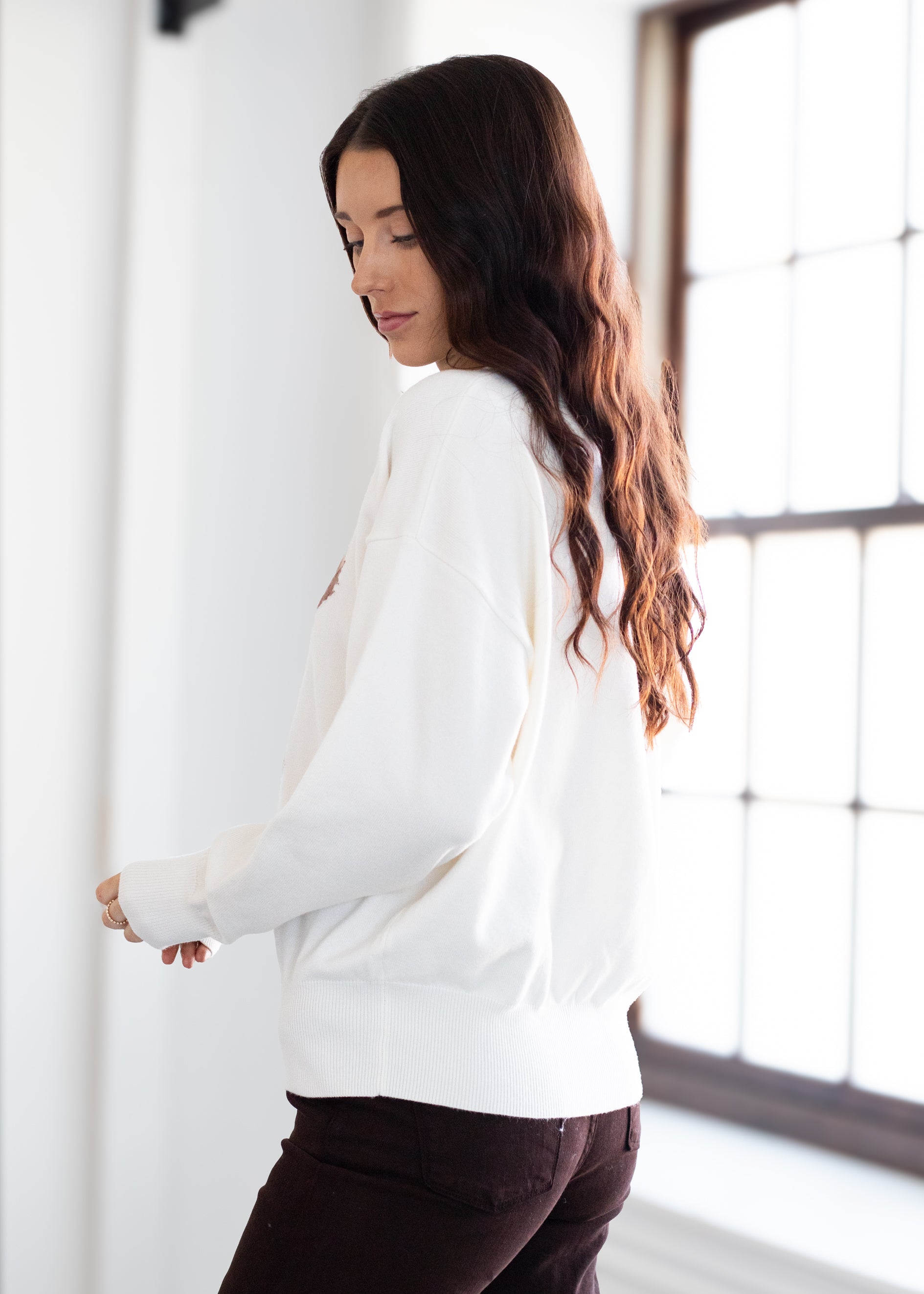 Woman wearing a white doodle sweater in a bright room with large windows.