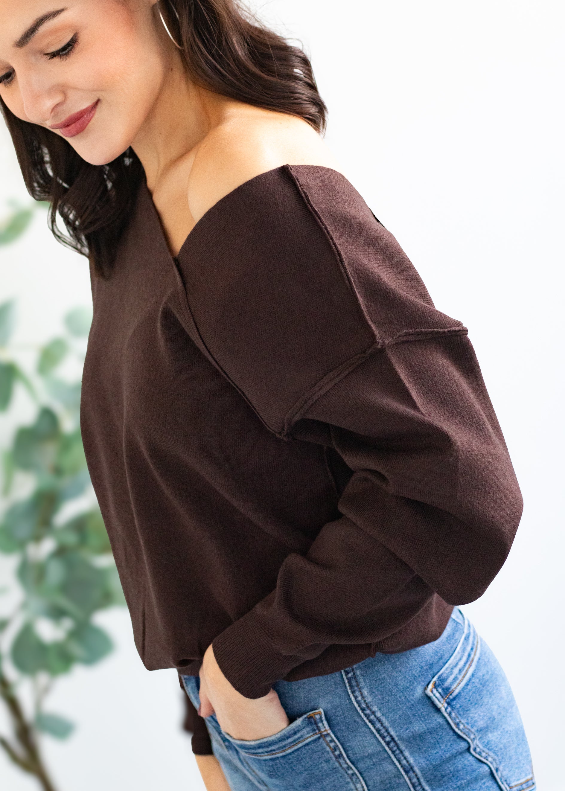Woman wearing a brown off-shoulder top and blue jeans against a blurred green background