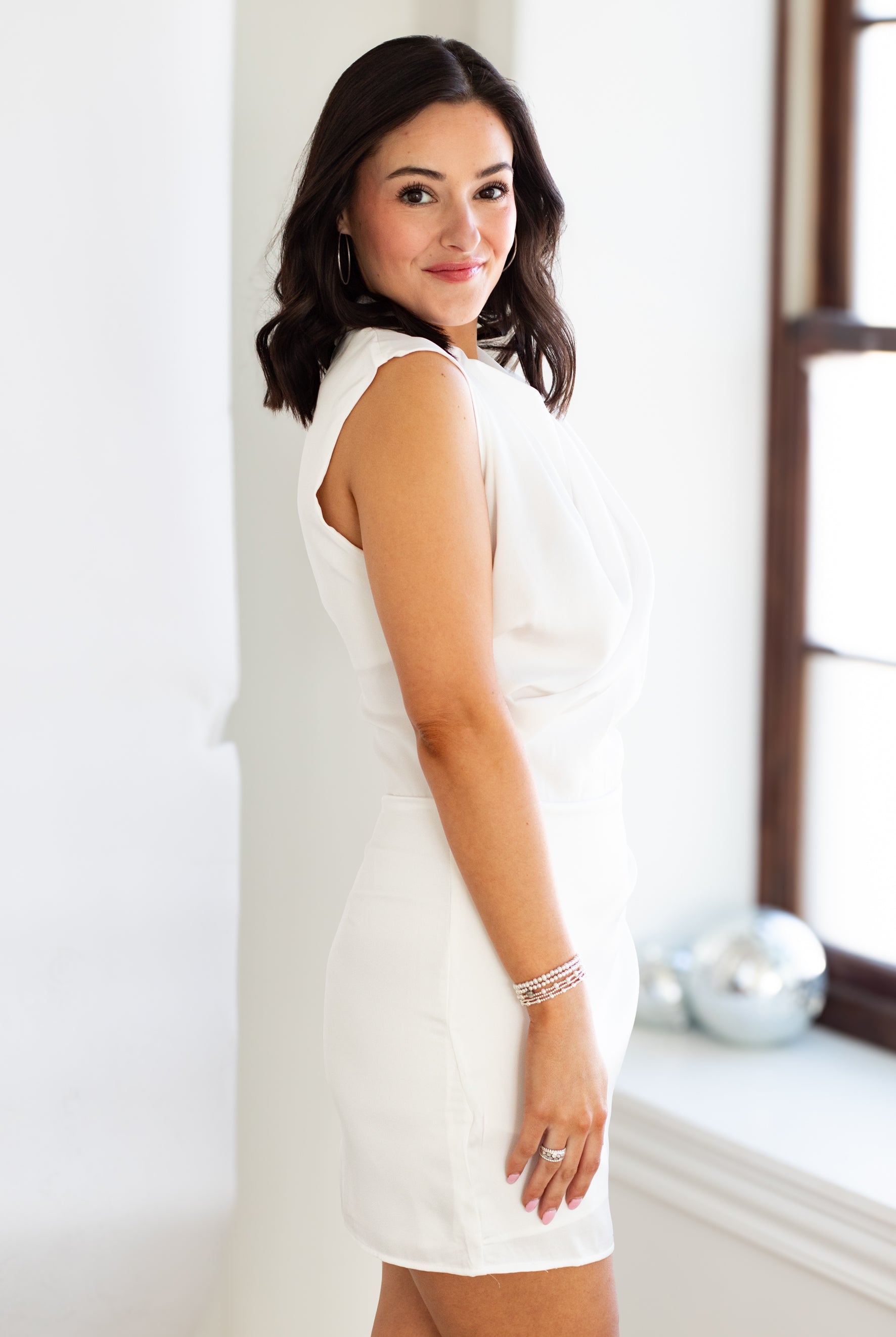 Woman wearing a white dress standing against a light-colored wall.