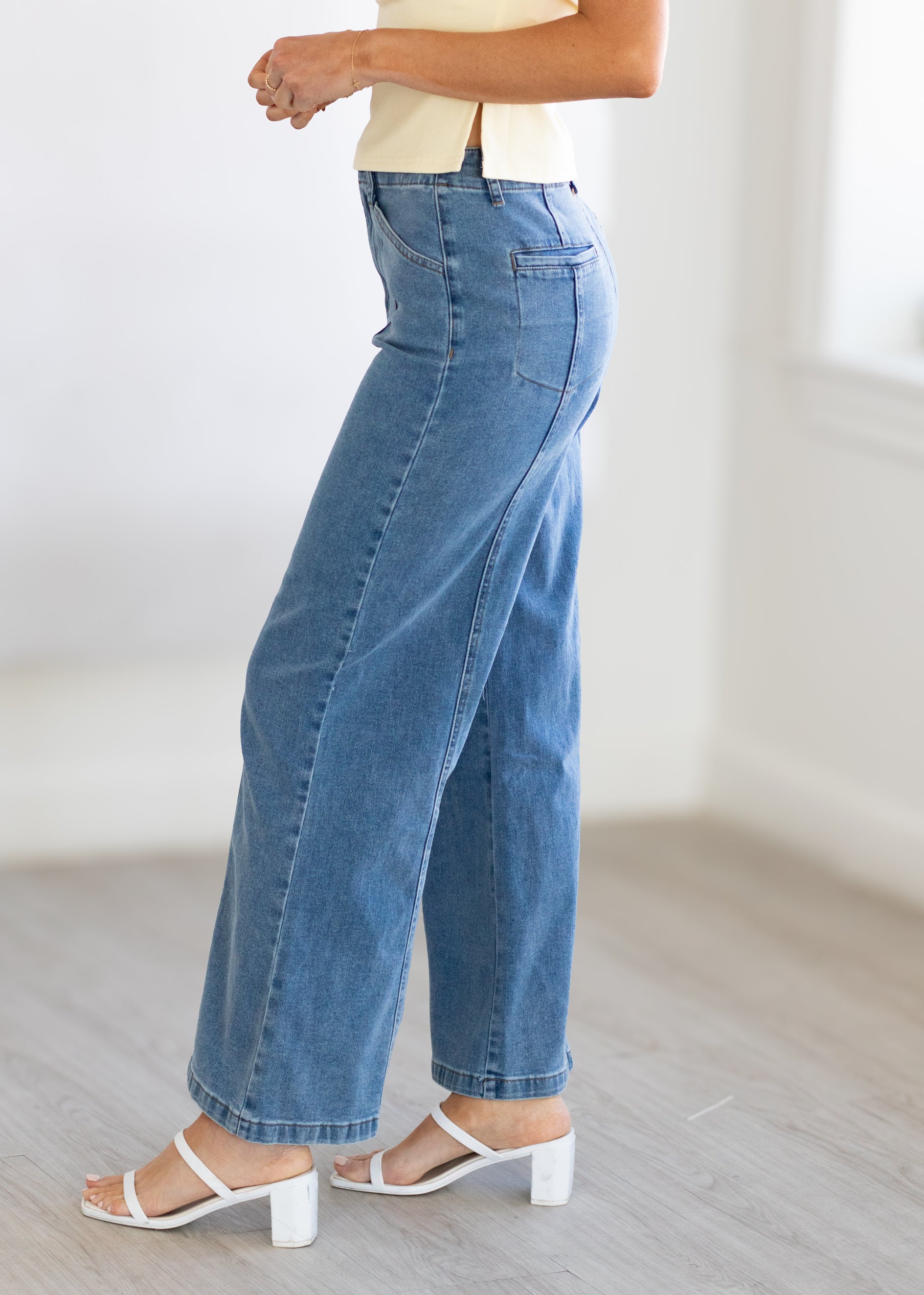 Person wearing blue jeans and white sandals on a light wooden floor.