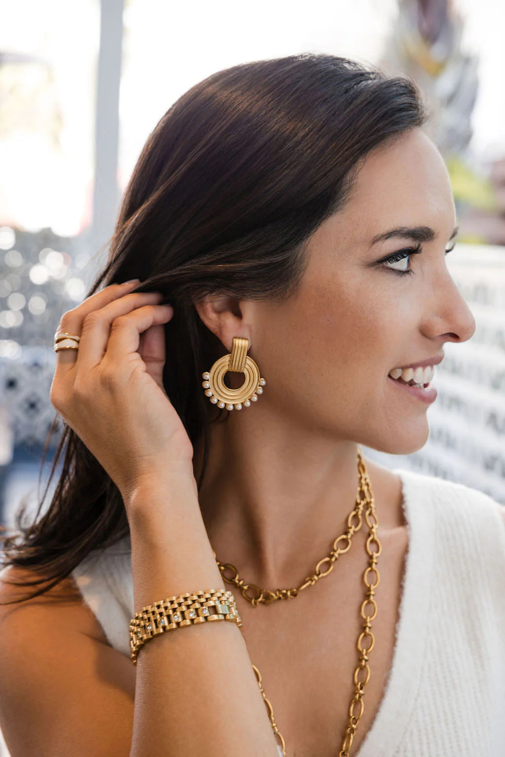 Woman wearing gold jewelry including earrings, necklace, and bracelet.