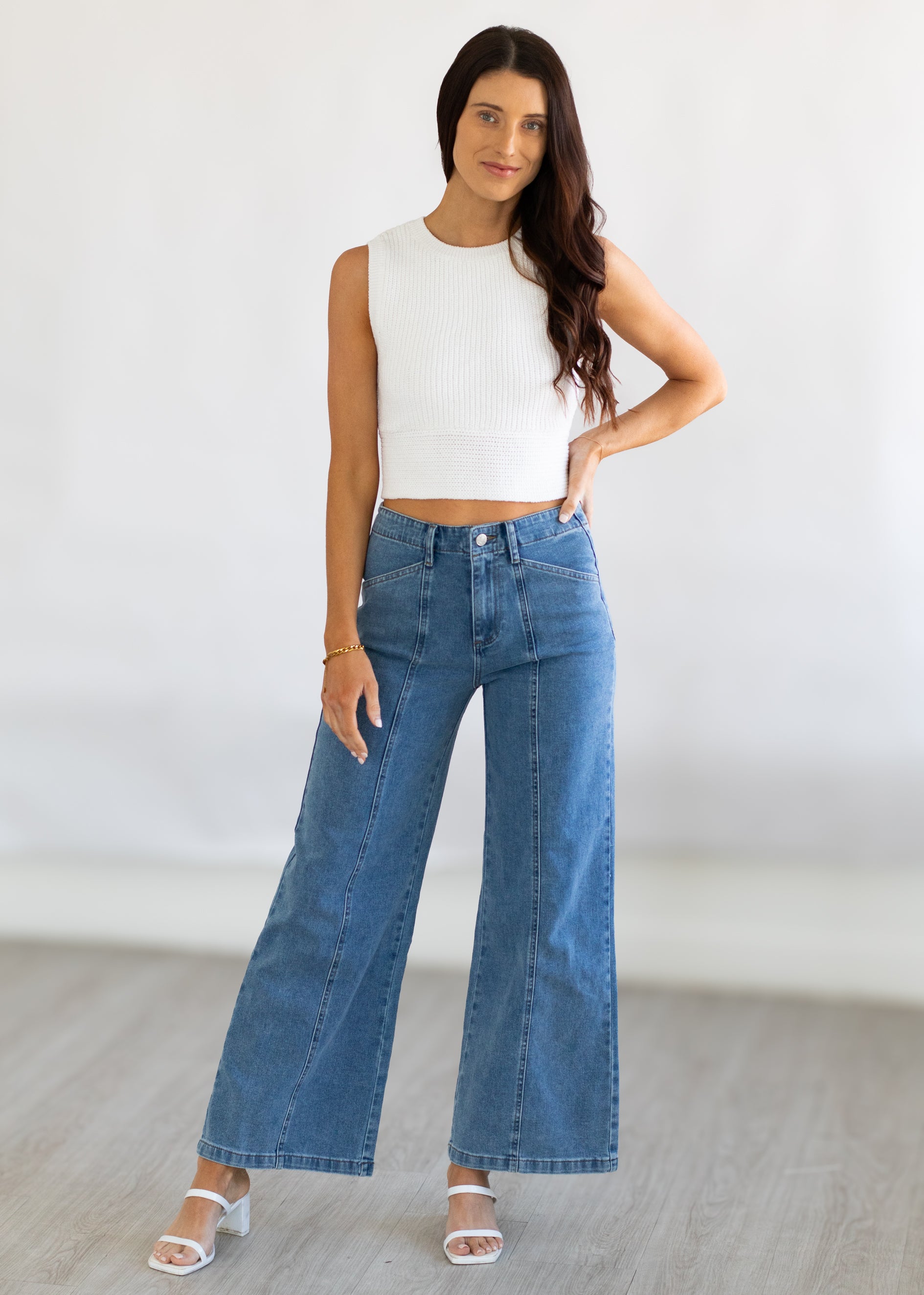 Woman wearing a white sleeveless top and blue jeans against a plain background