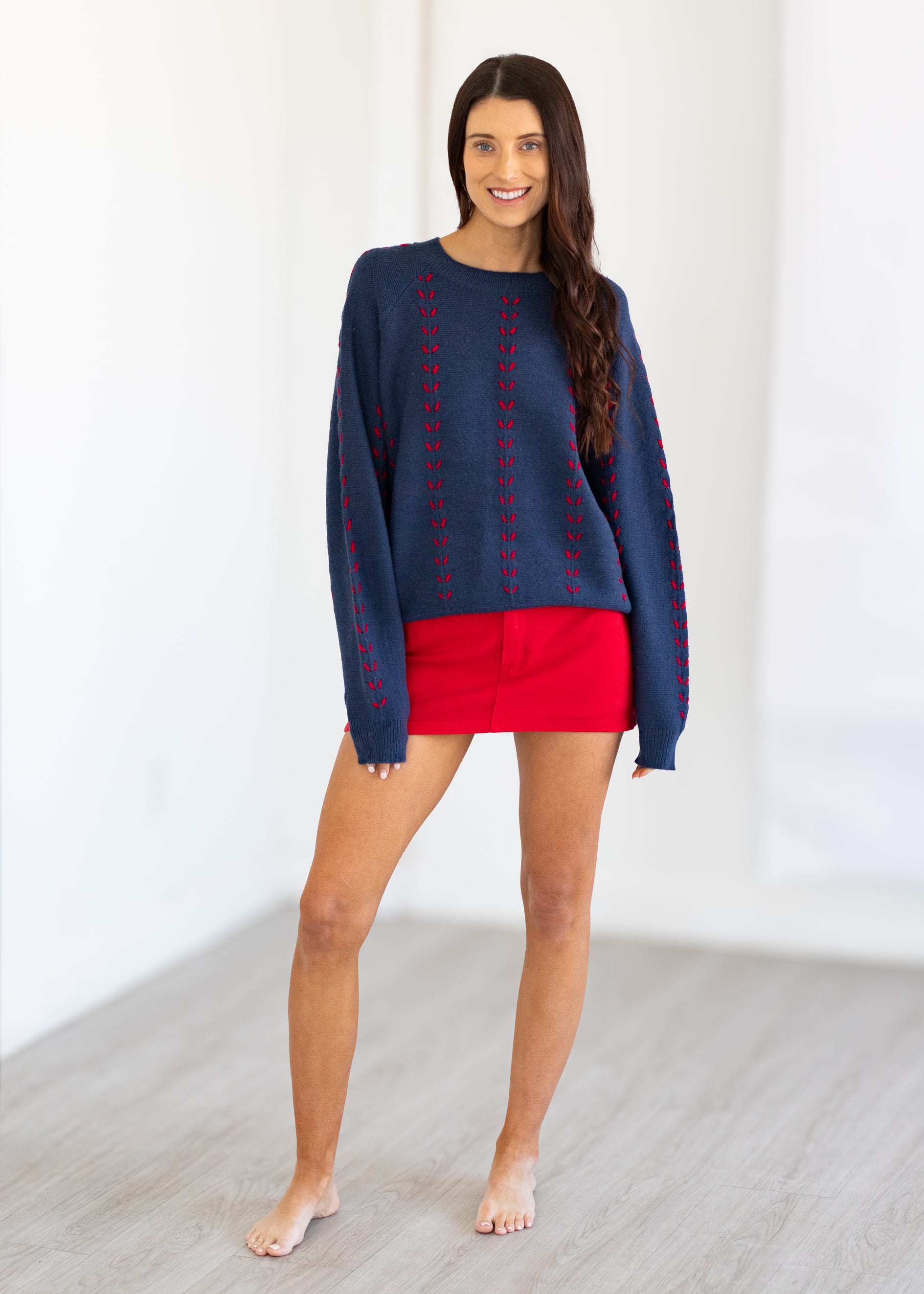 Woman wearing a navy sweater with red accents and red shorts on a white background
