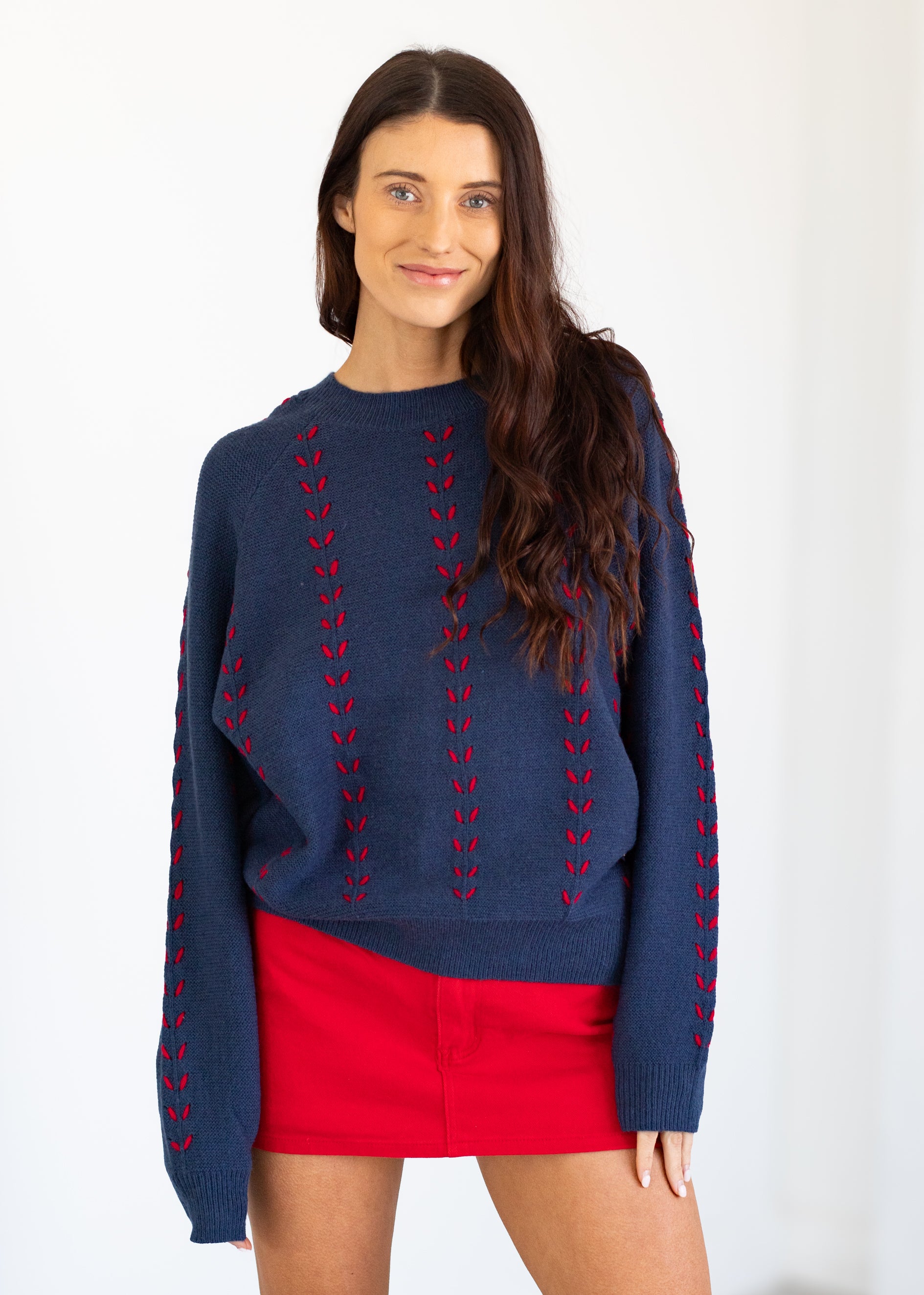 Woman wearing a blue sweater with red patterns and a red skirt on a white background