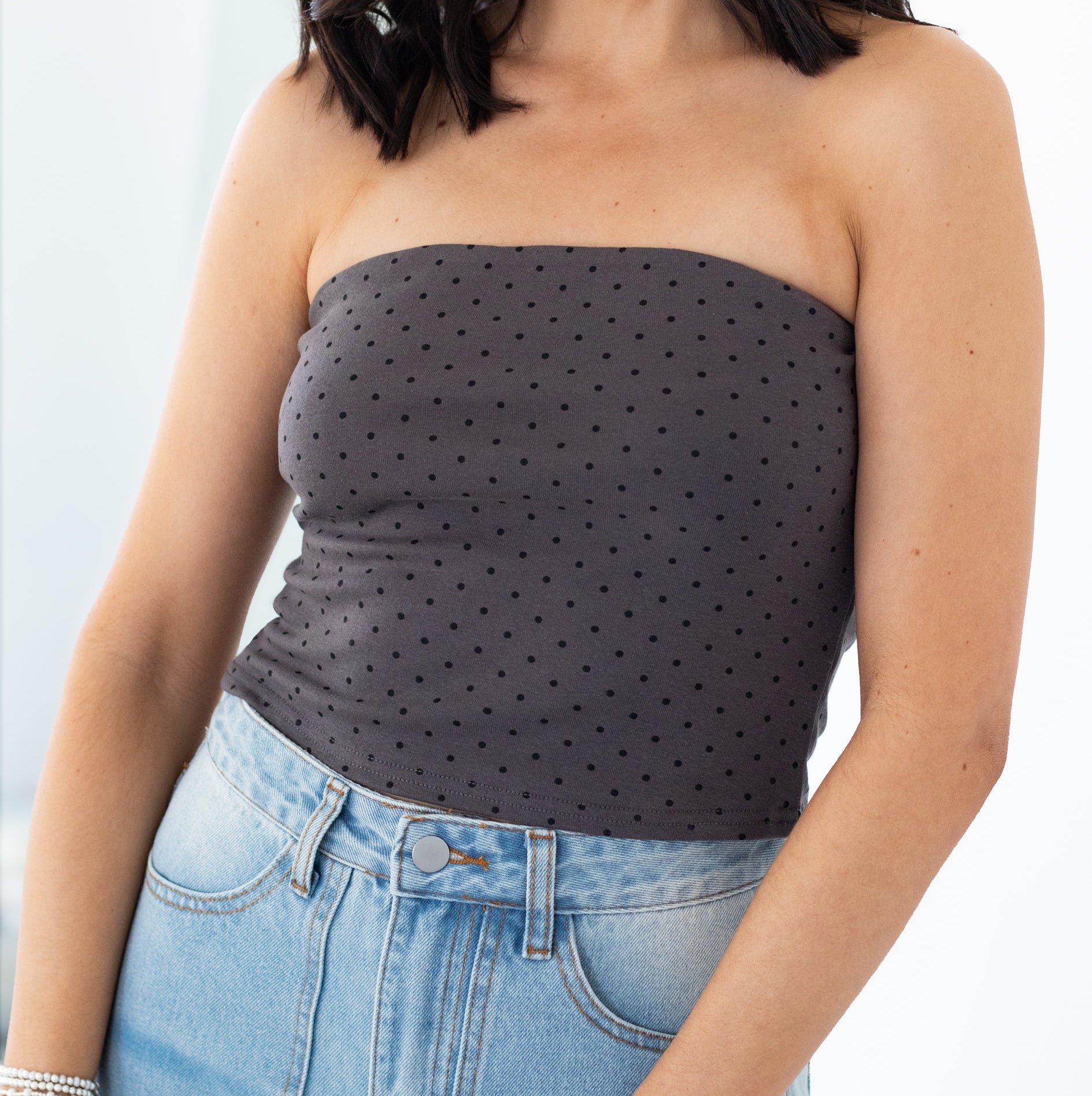 Woman wearing a strapless polka dot top and jeans on a white background